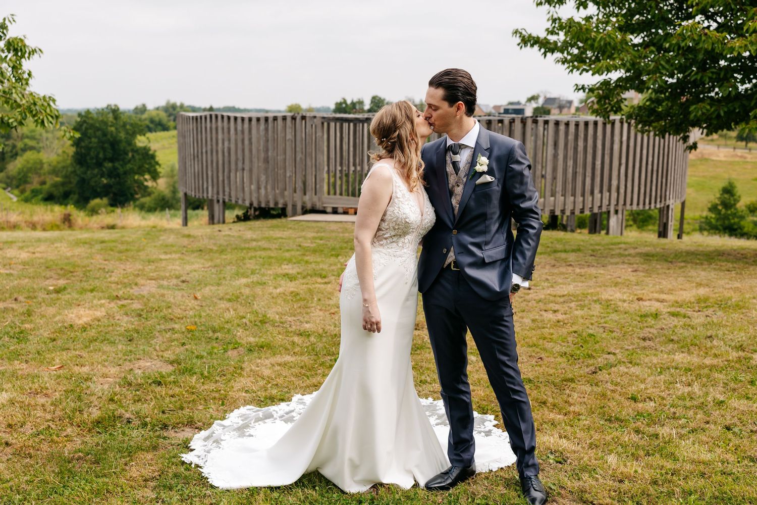 Bride and groom sharing a gentle kiss while standing on a green lawn with a wooden structure behind them.