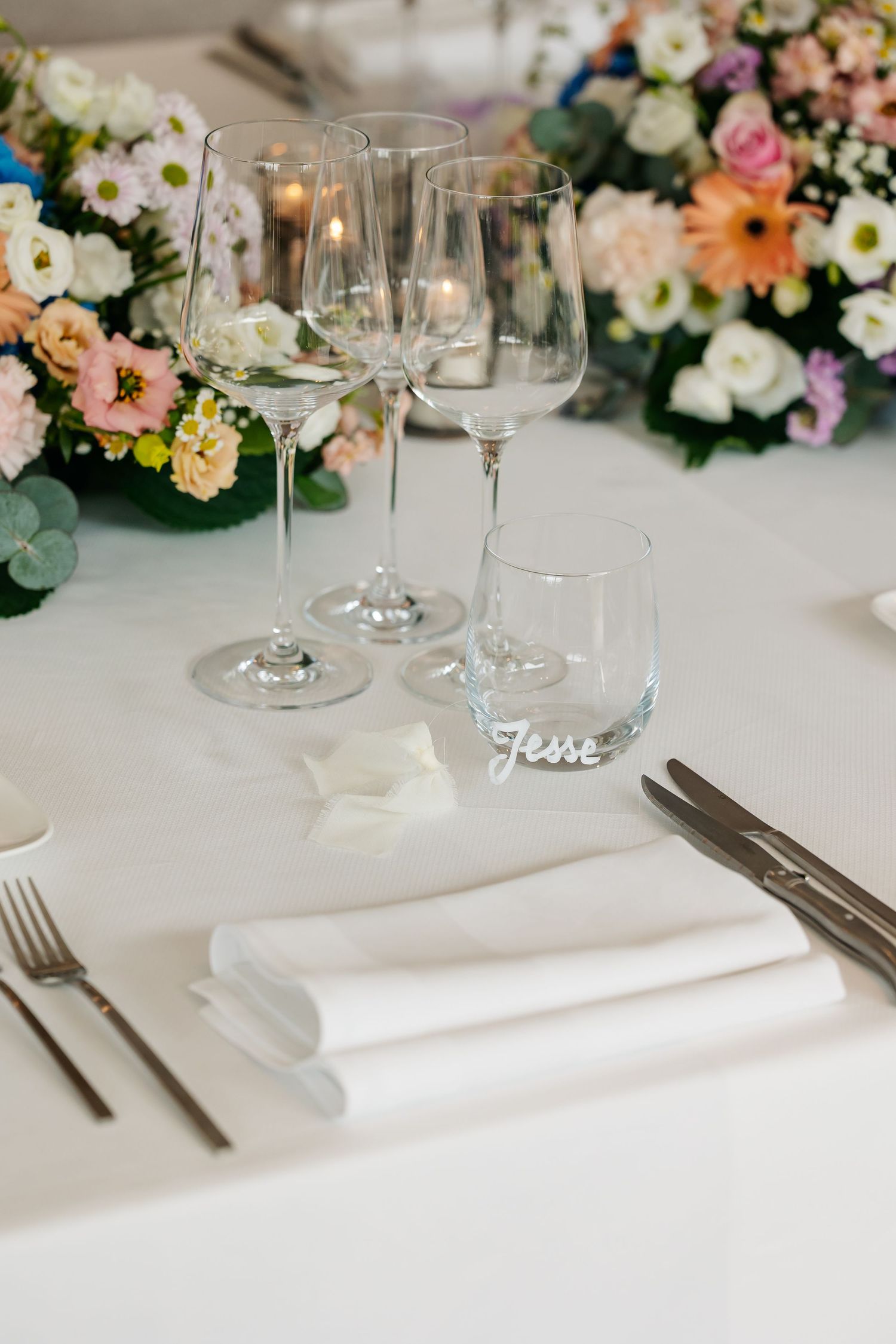 Elegant wedding table setting with crystal glasses, white napkin, and a personalized name card reading Jesse.