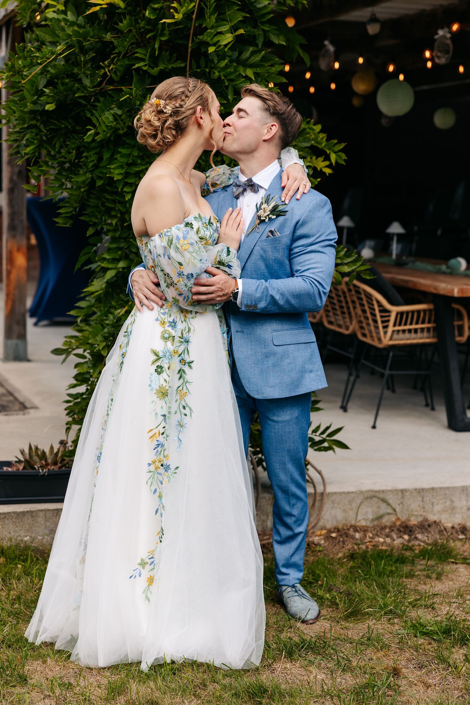 Bride and groom sharing a romantic kiss in lush garden at dusk.