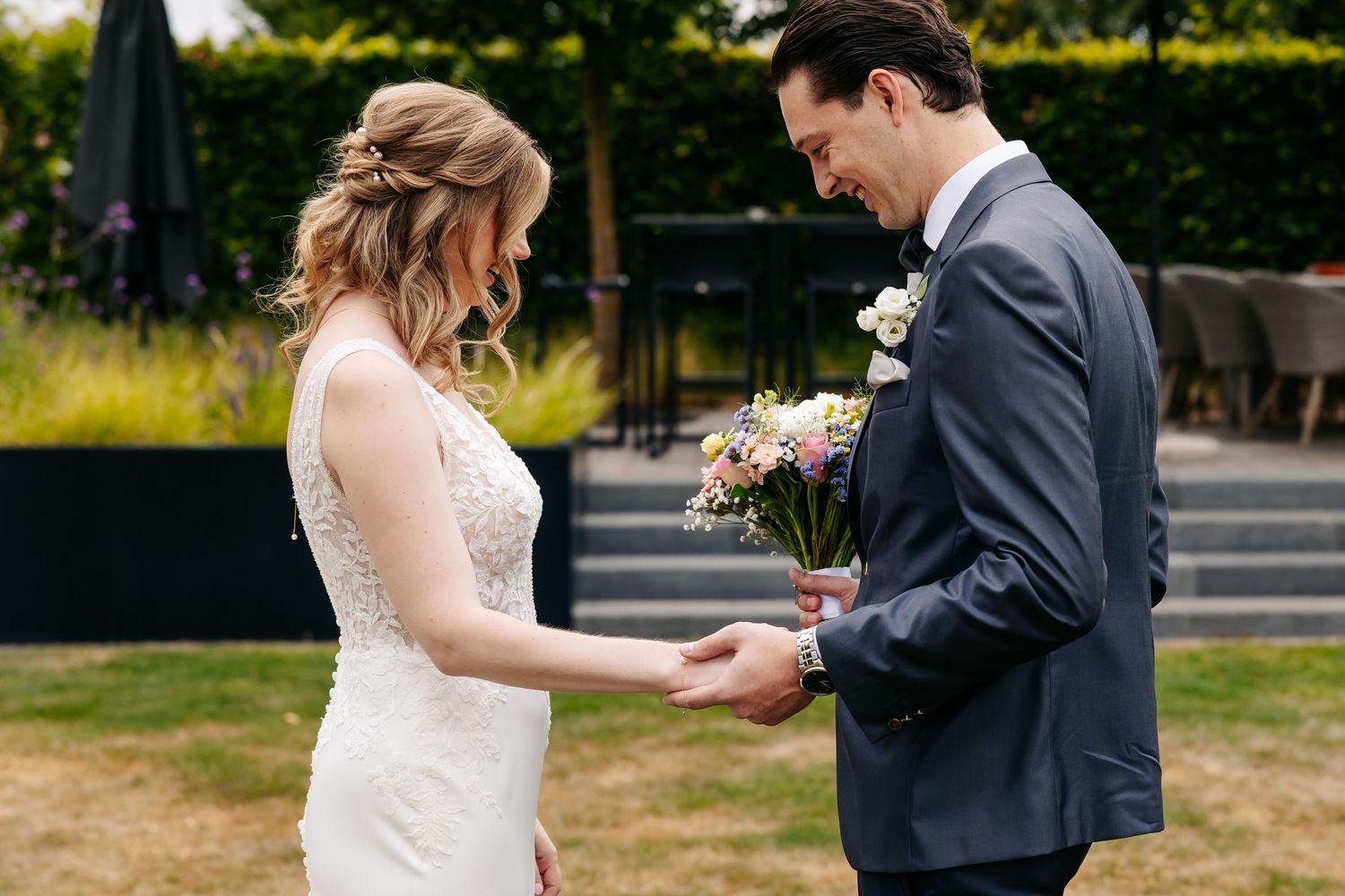Bride and groom share an intimate first look moment, exchanging a small bouquet outdoors at a garden wedding venue.