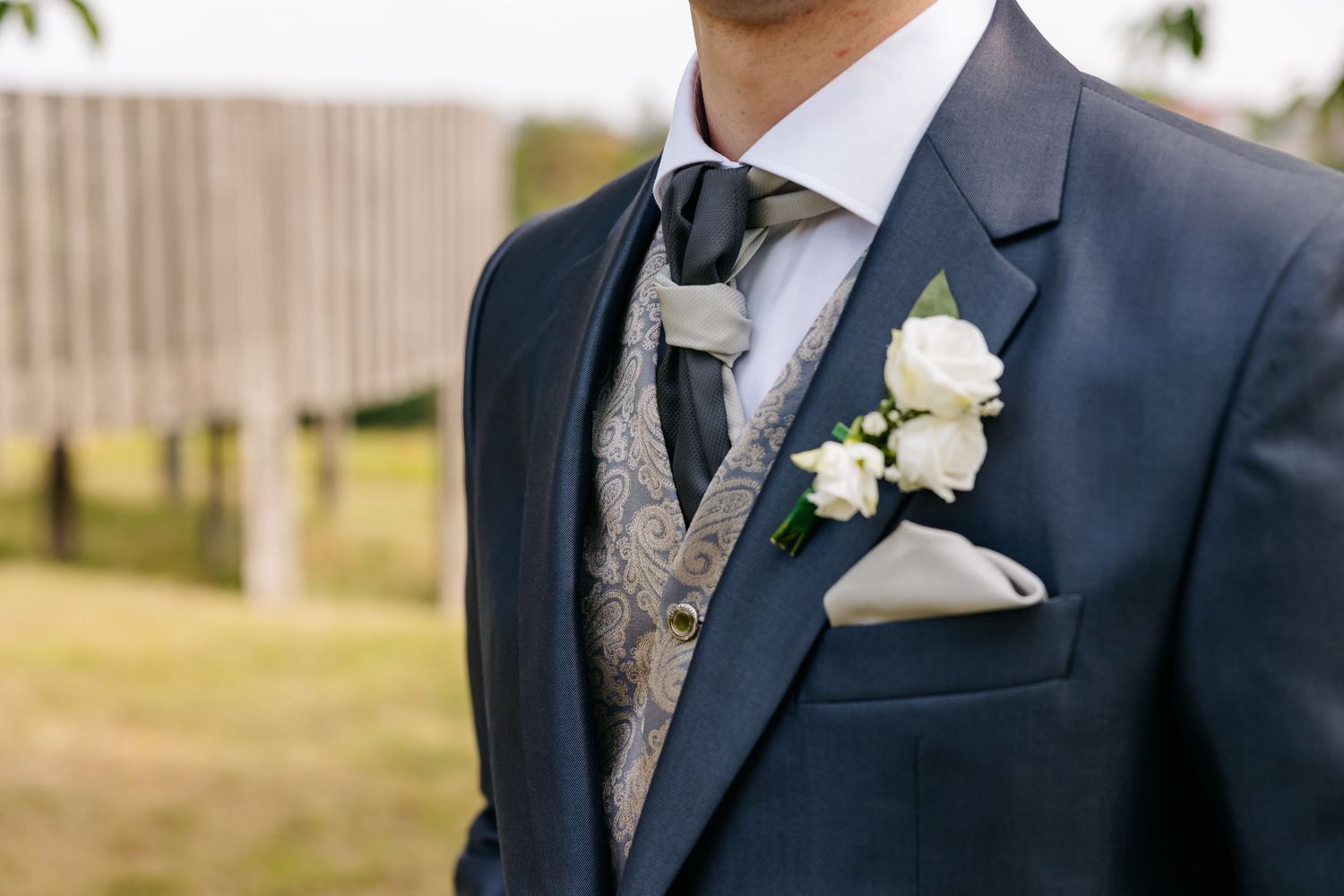 Close-up of groom in navy suit with paisley vest, white boutonniere, and pocket square.