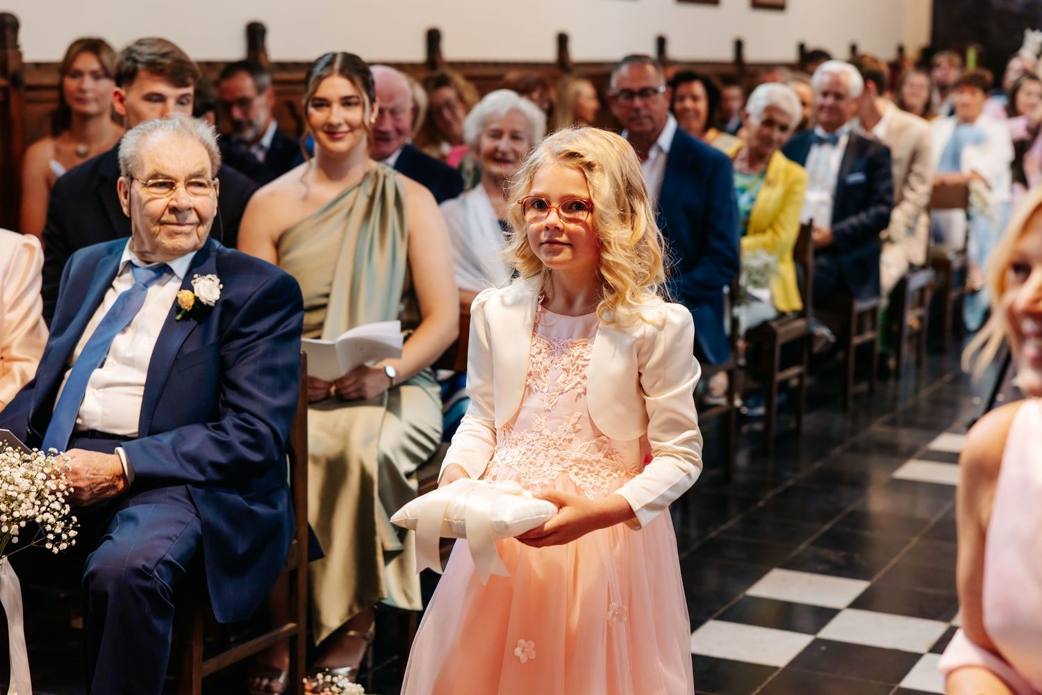Smiling flower girl carrying ring pillow down wedding ceremony aisle.