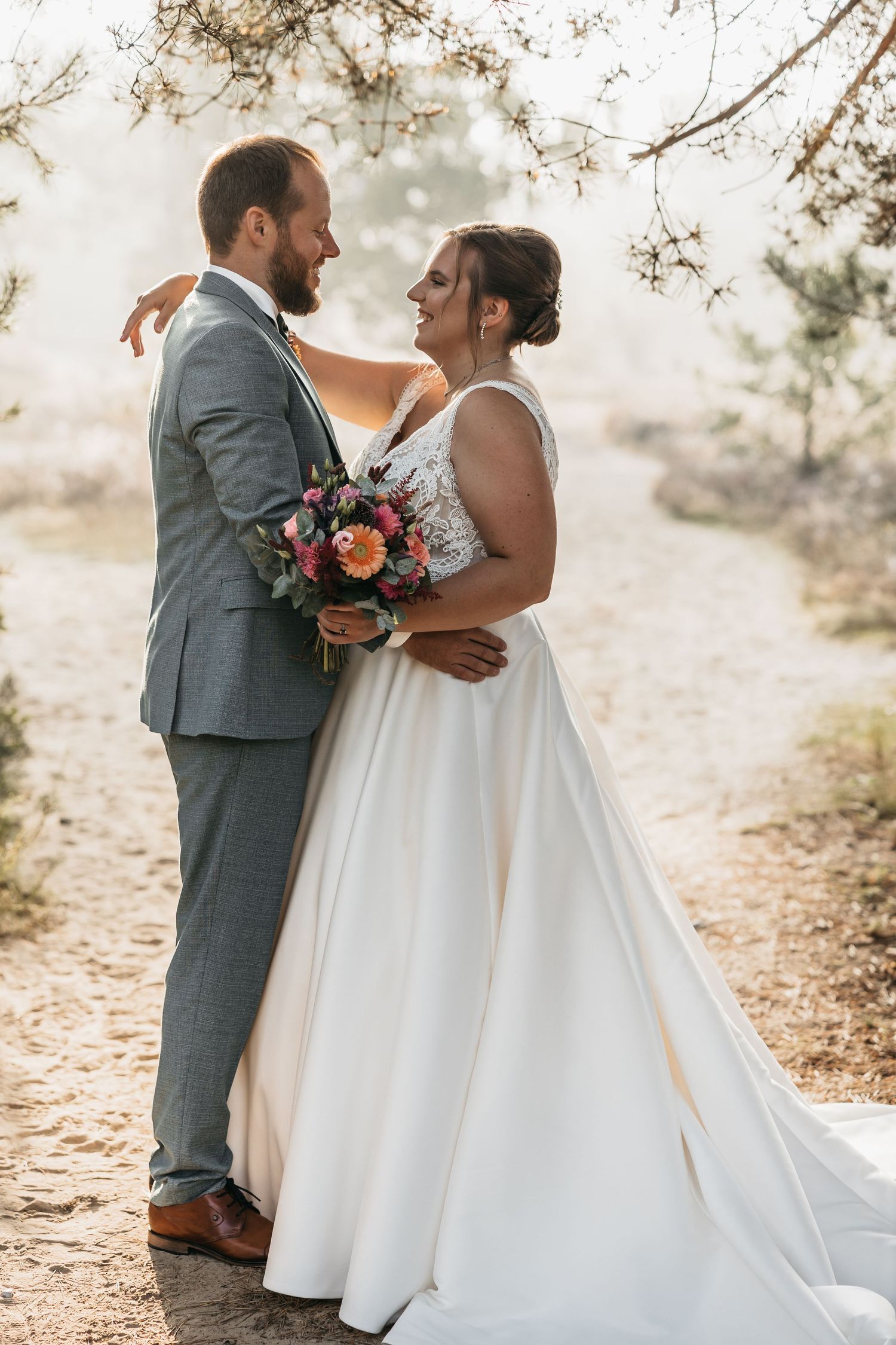 Bride and groom embrace on a misty forest path in wedding attire.