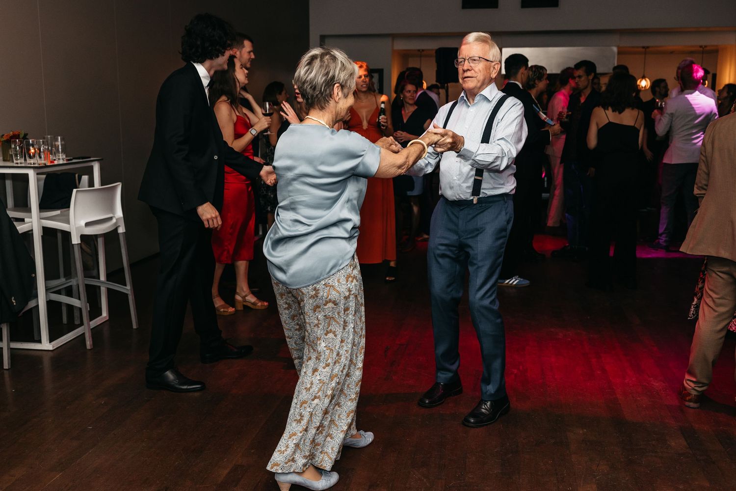 Senior couple dancing together on colorful lit wedding reception dance floor.