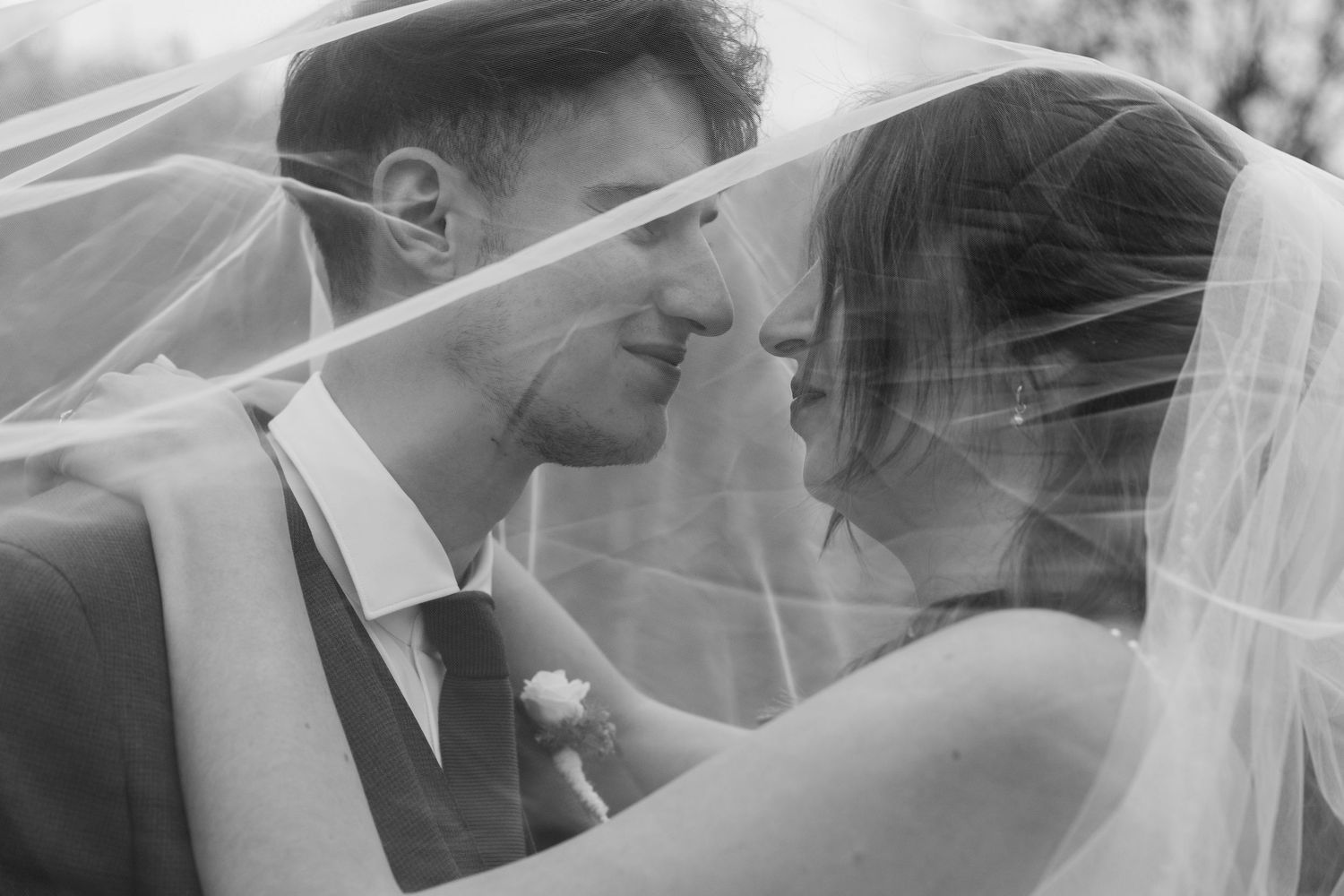 Romantic black and white photo of bride and groom beneath a flowing veil on their wedding day.