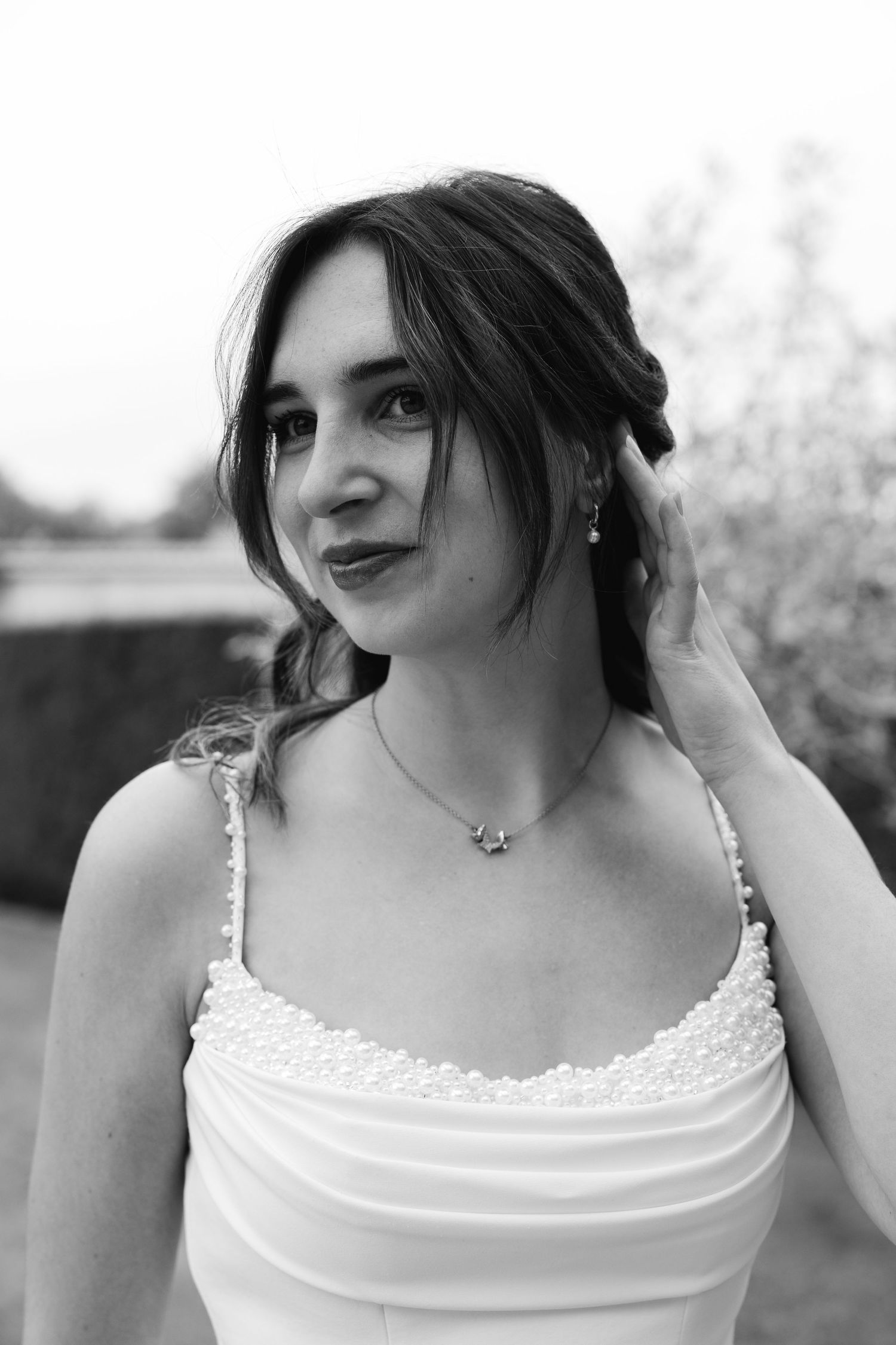 Elegant bride in a white pearl-strap gown poses in a black and white portrait outdoors.
