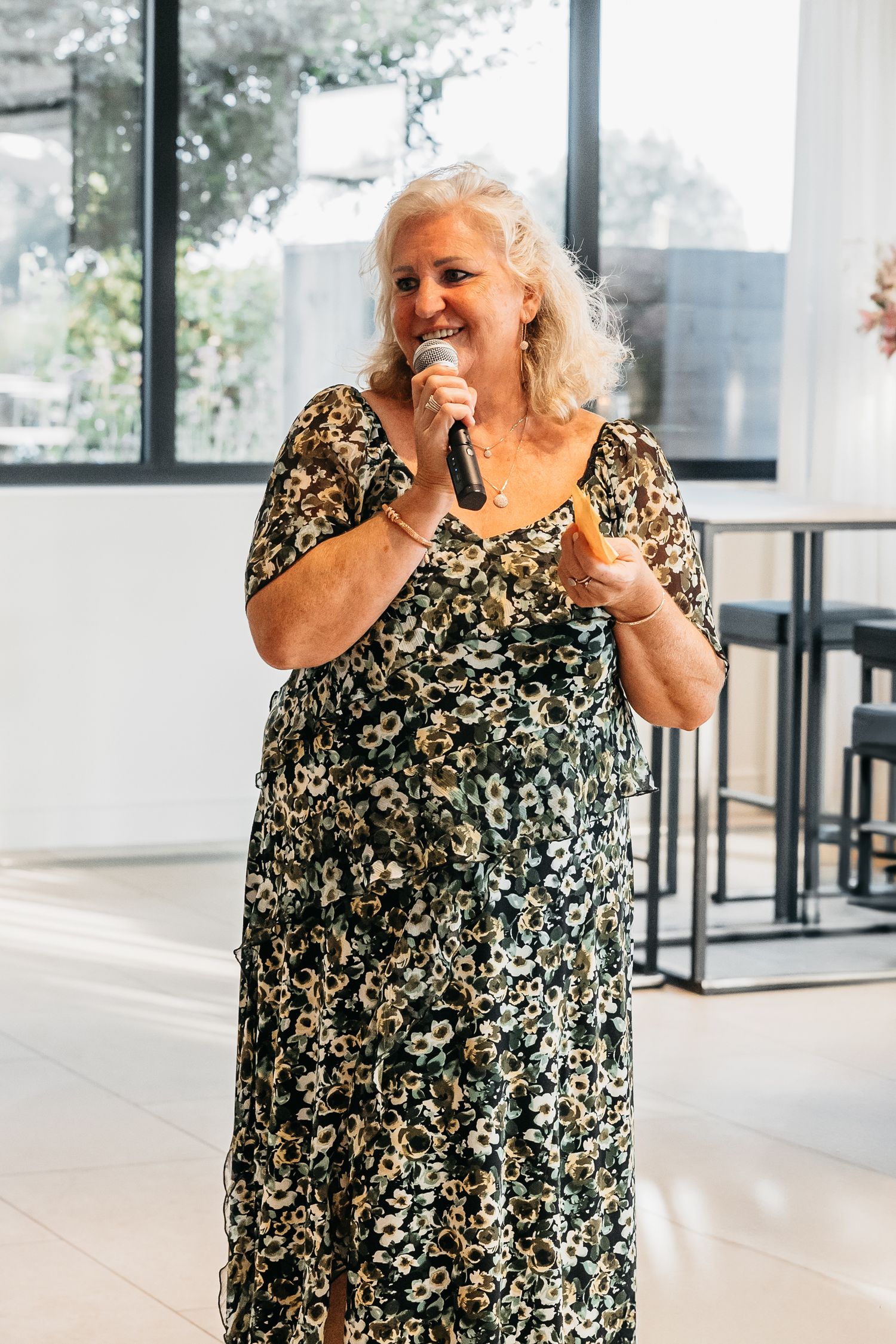 Older woman in a floral dress giving a heartfelt speech with a microphone at a wedding.