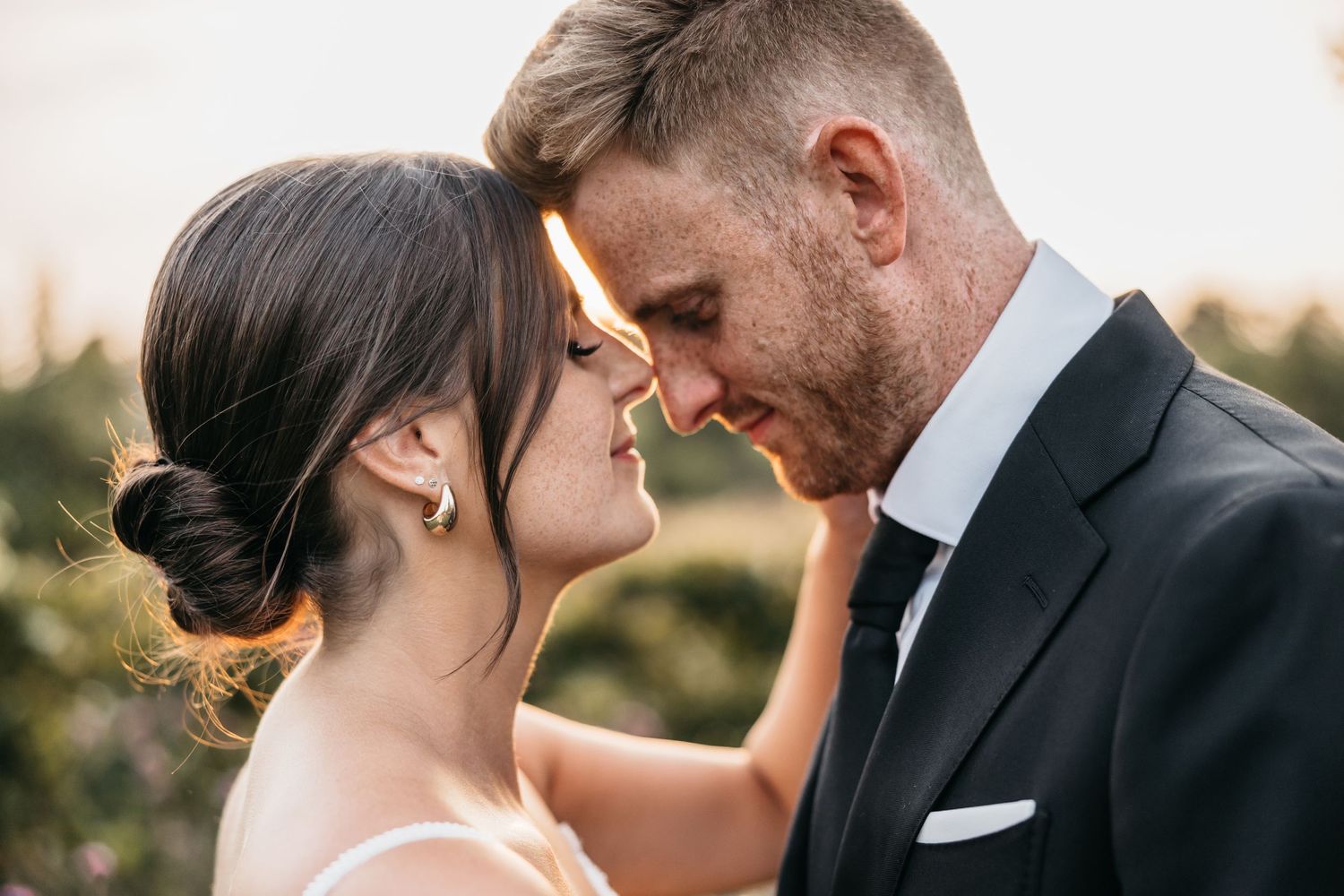 Bride and groom share an intimate forehead touch at sunset outdoors.