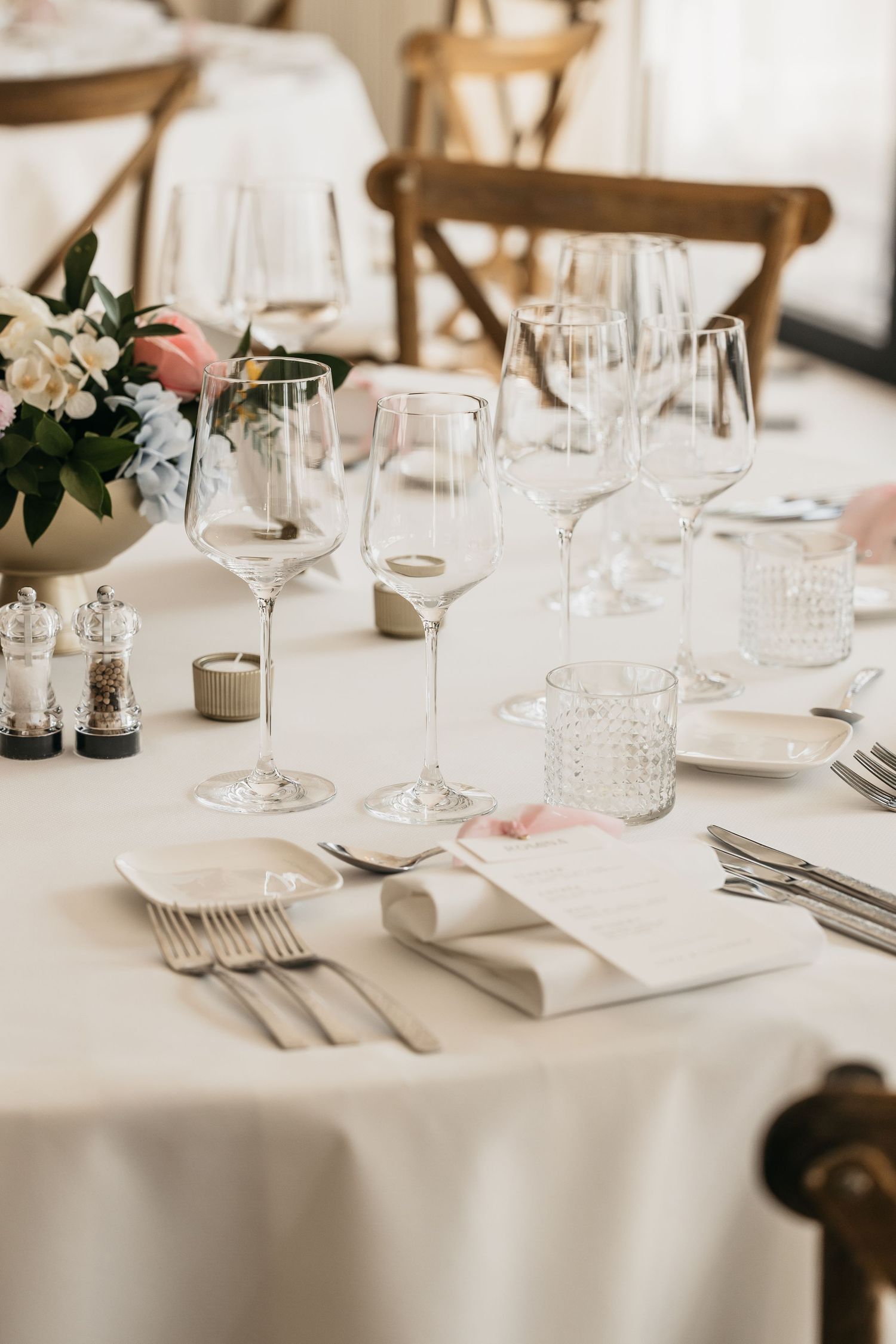 Elegant wedding table setting featuring crystal wine glasses, white linens, and pink floral arrangement.