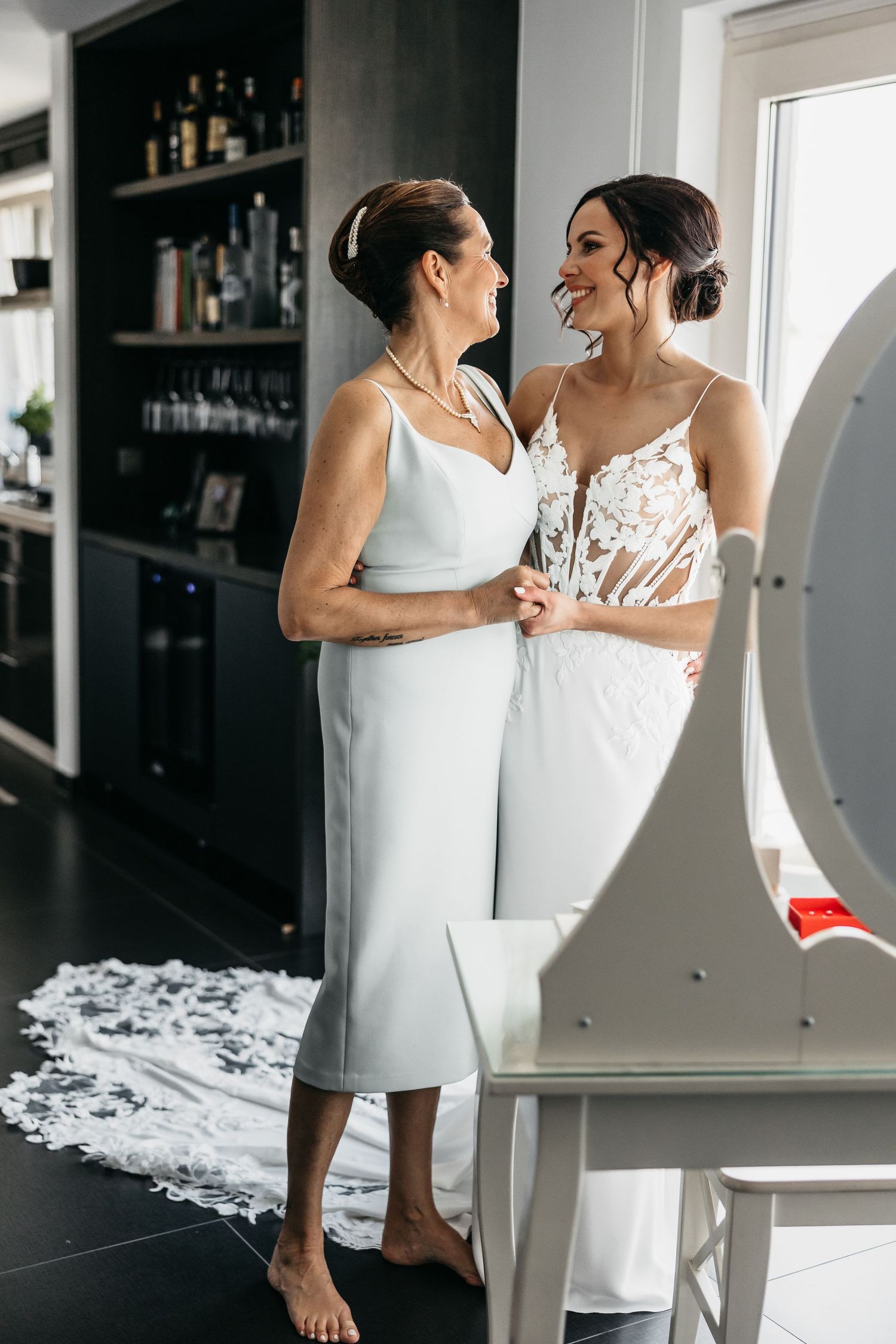 Bride and mother sharing a tender smile in elegant dresses before wedding.