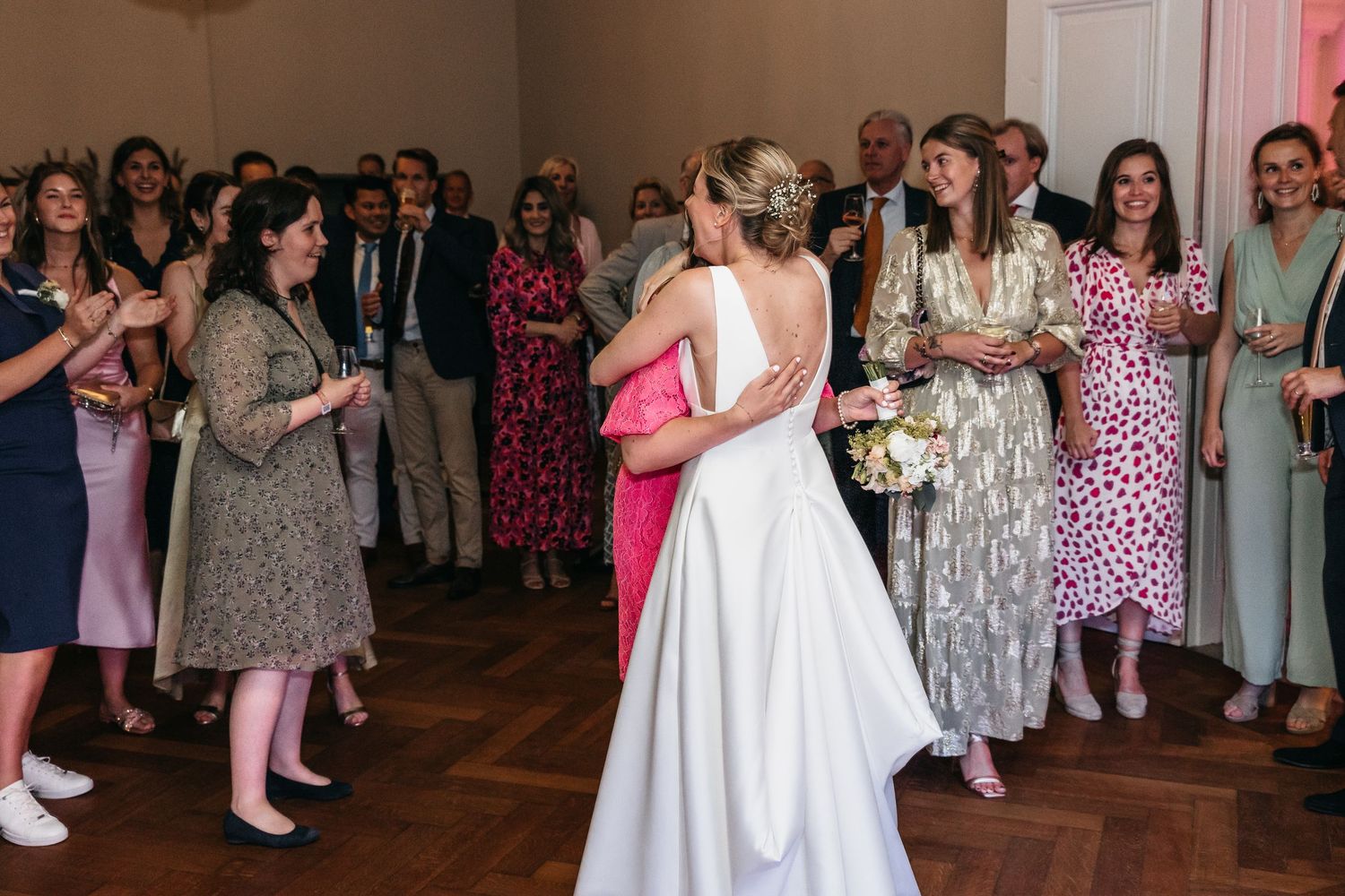 Bride in white gown hugging a guest during wedding reception celebration.