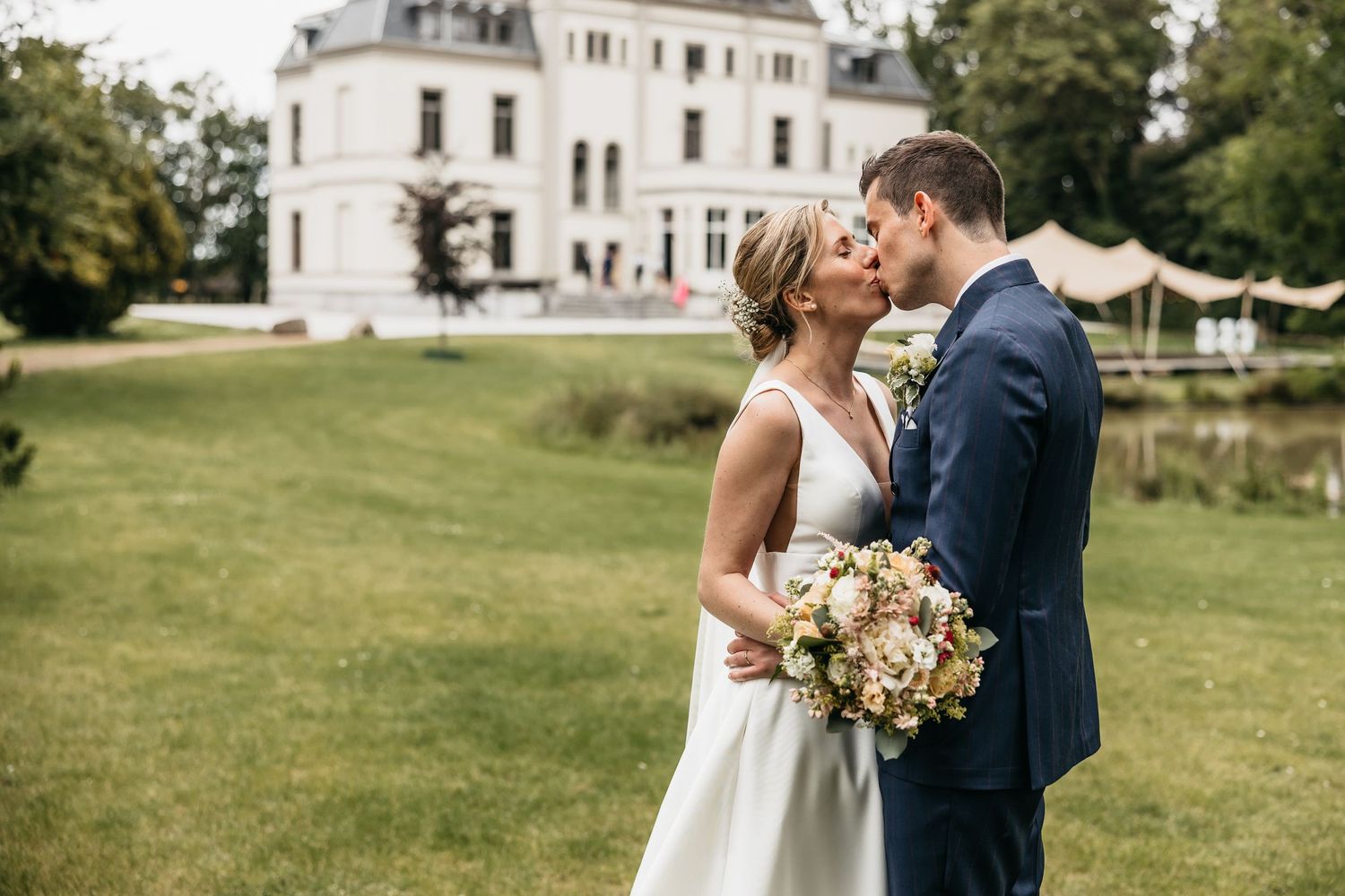 Bride and groom kissing on a green lawn with a white chateau in the background.