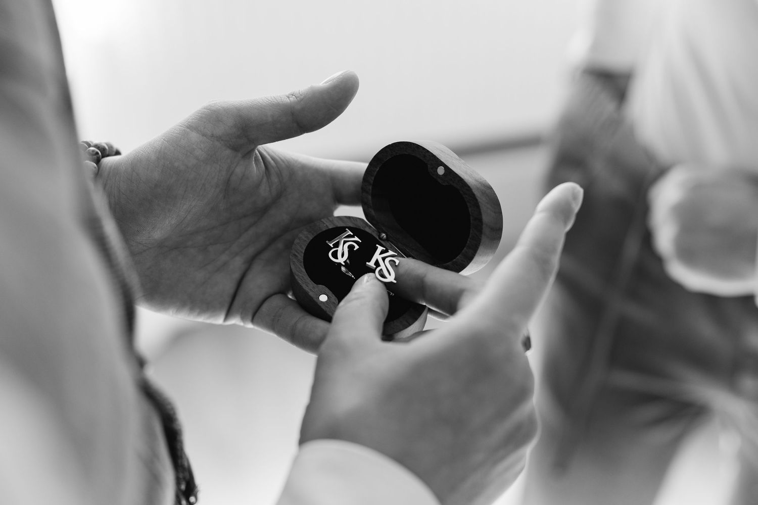 Black and white photo of hands holding open wooden ring box containing wedding rings.