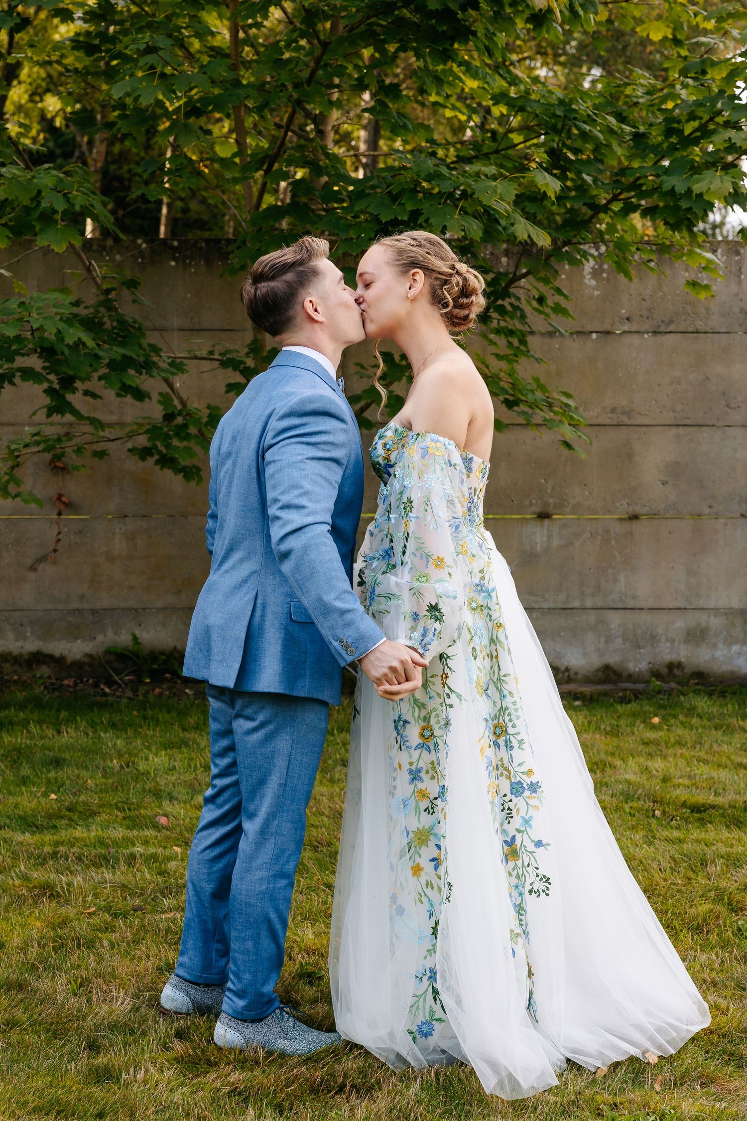 Bride and groom share a kiss in garden, bride wearing floral embroidered wedding dress.