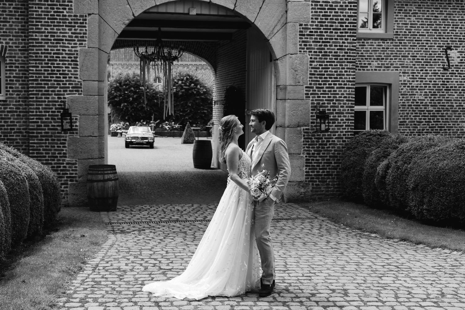 Black and white photo of bride and groom embracing in cobblestone courtyard of elegant brick wedding venue.