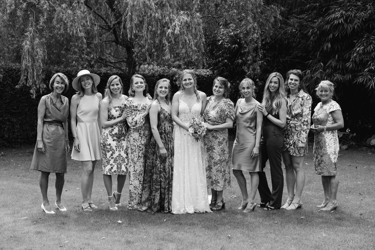 Black and white photo of a bride with a large group of women posing outdoors under a willow tree.
