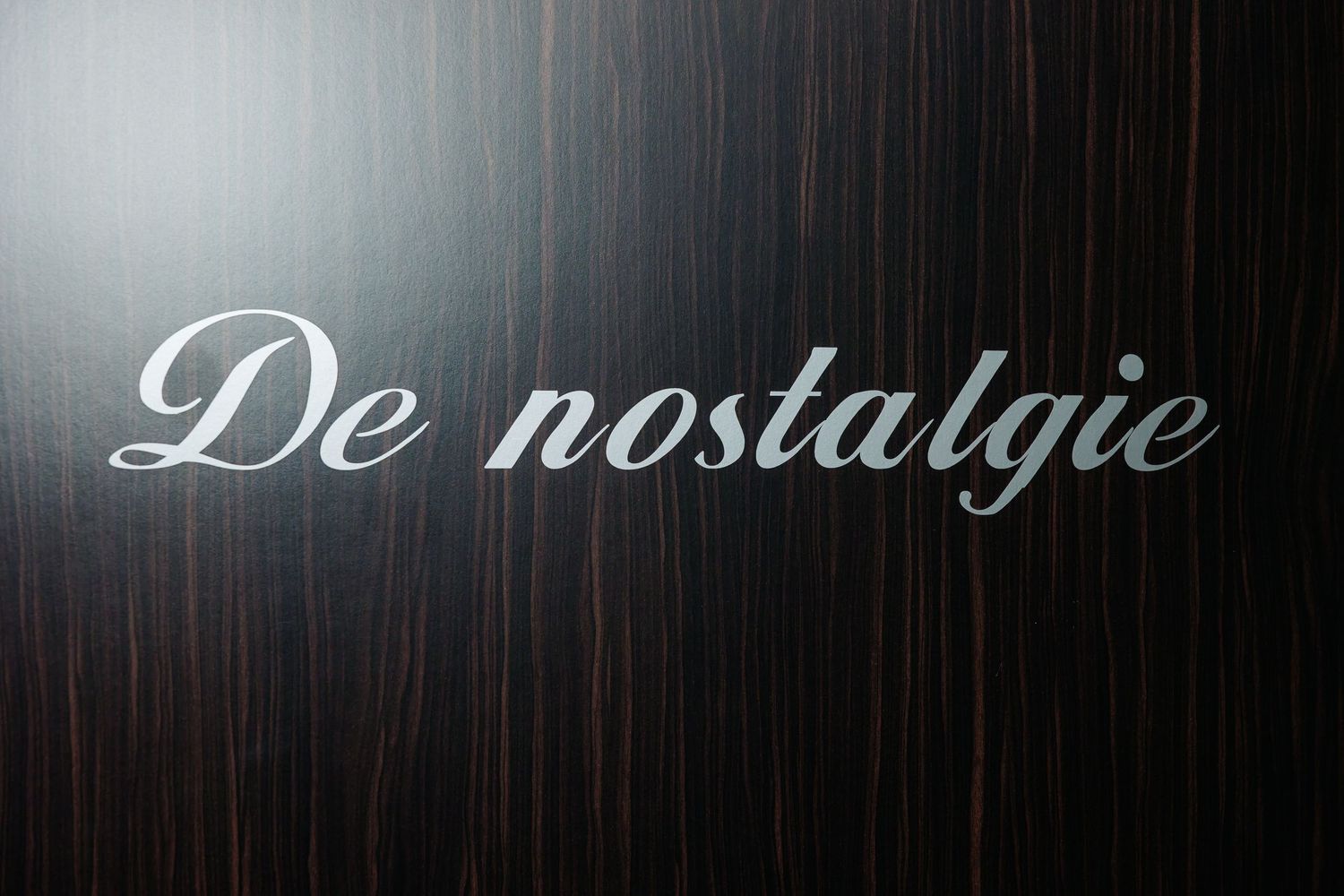 De Nostalgie wedding venue sign in silver script on dark wood panel.