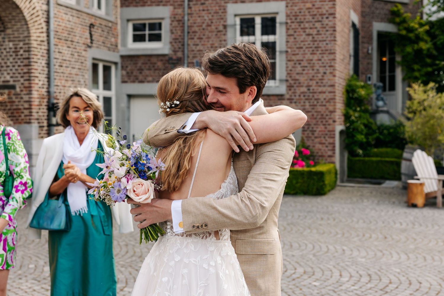 Bride and groom sharing emotional first look hug outdoors at elegant brick estate venue.