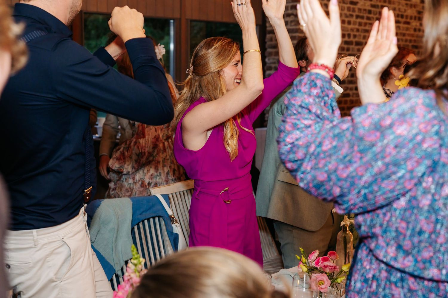 Woman in purple dress dances with raised arms at a lively indoor wedding reception.
