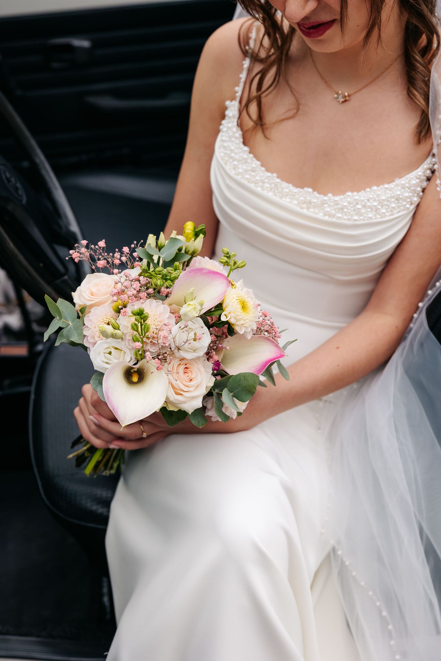 Close-up of bride in pearl-adorned white dress holding bouquet of calla lilies and roses.