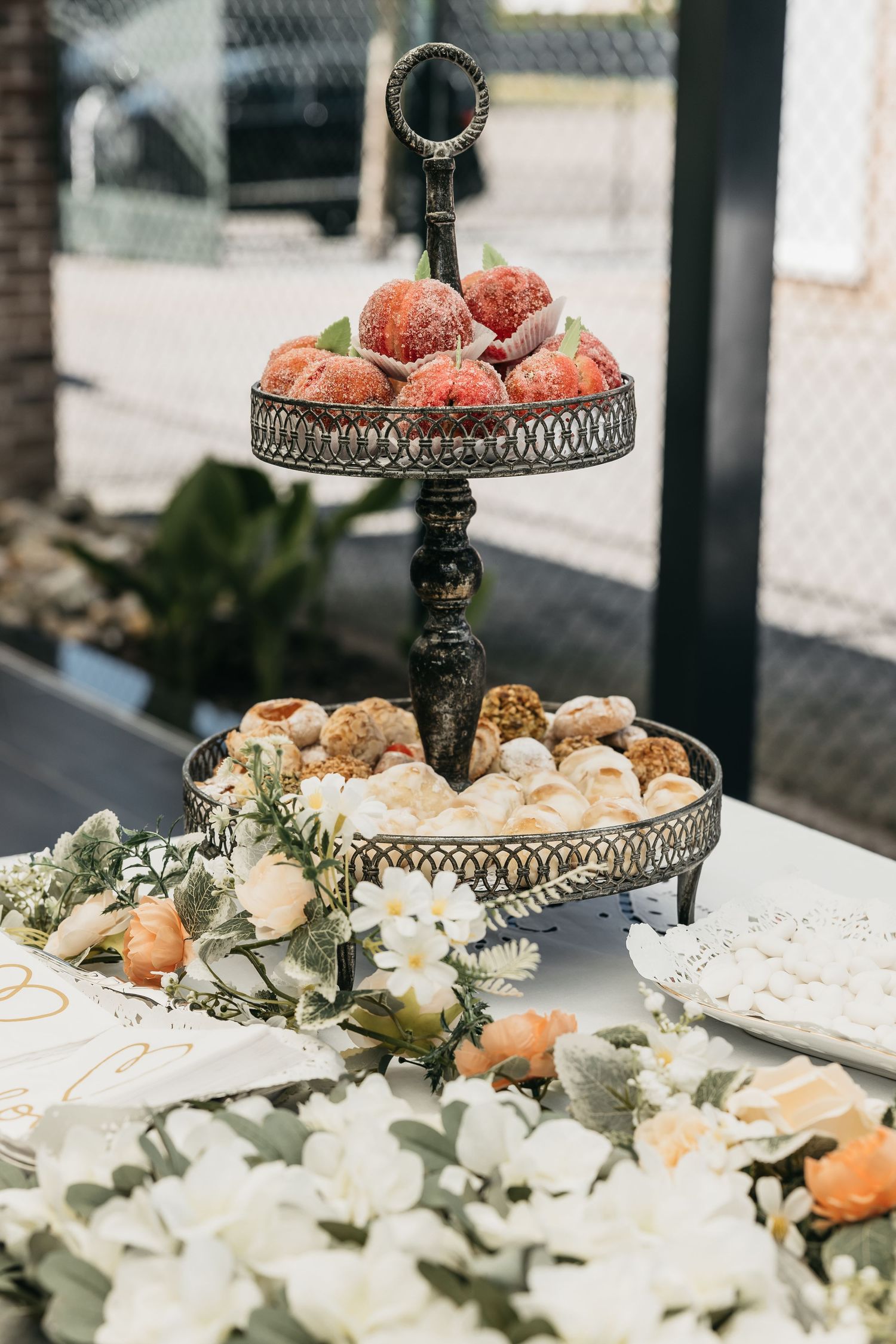 Two-tiered vintage dessert stand with strawberries and pastries surrounded by white flowers.