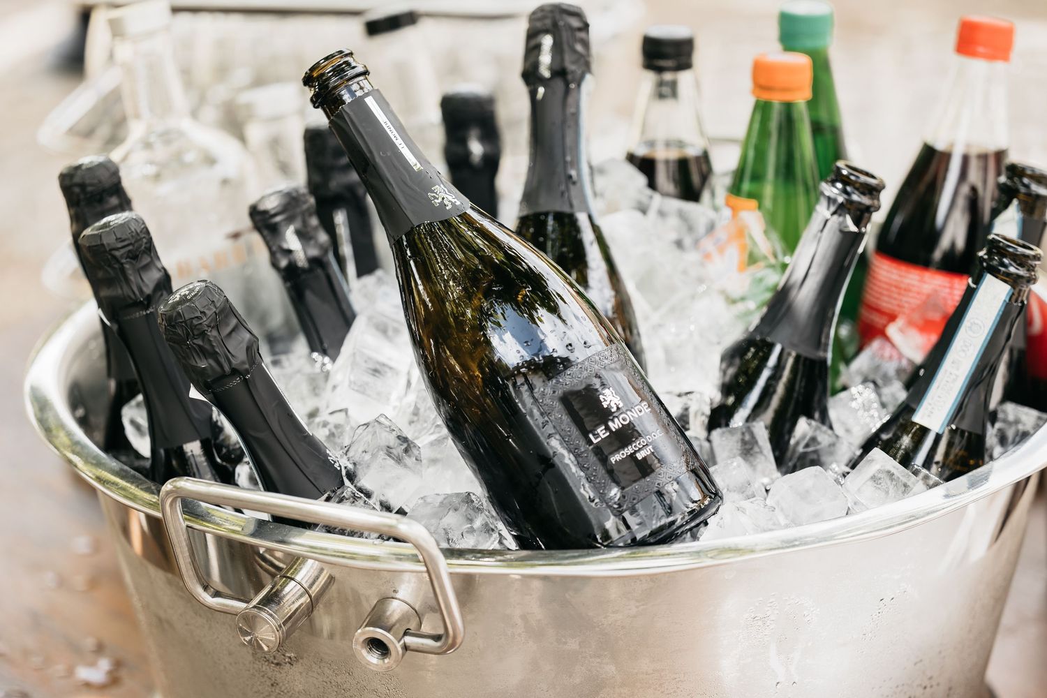 Champagne and beverage bottles chilling in ice-filled silver bucket at wedding reception.