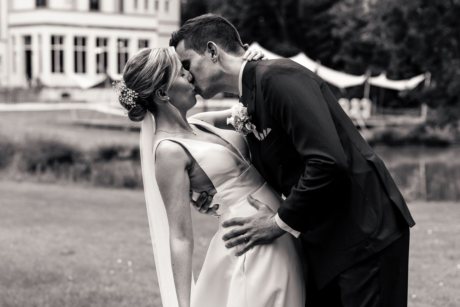 Black and white photo of bride and groom sharing a romantic kiss on garden lawn.
