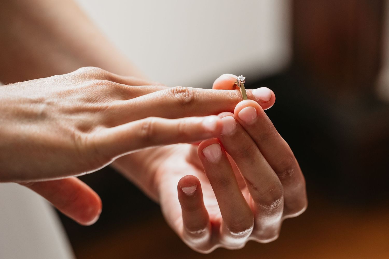 Close-up of groom placing a diamond engagement ring onto bride's finger.