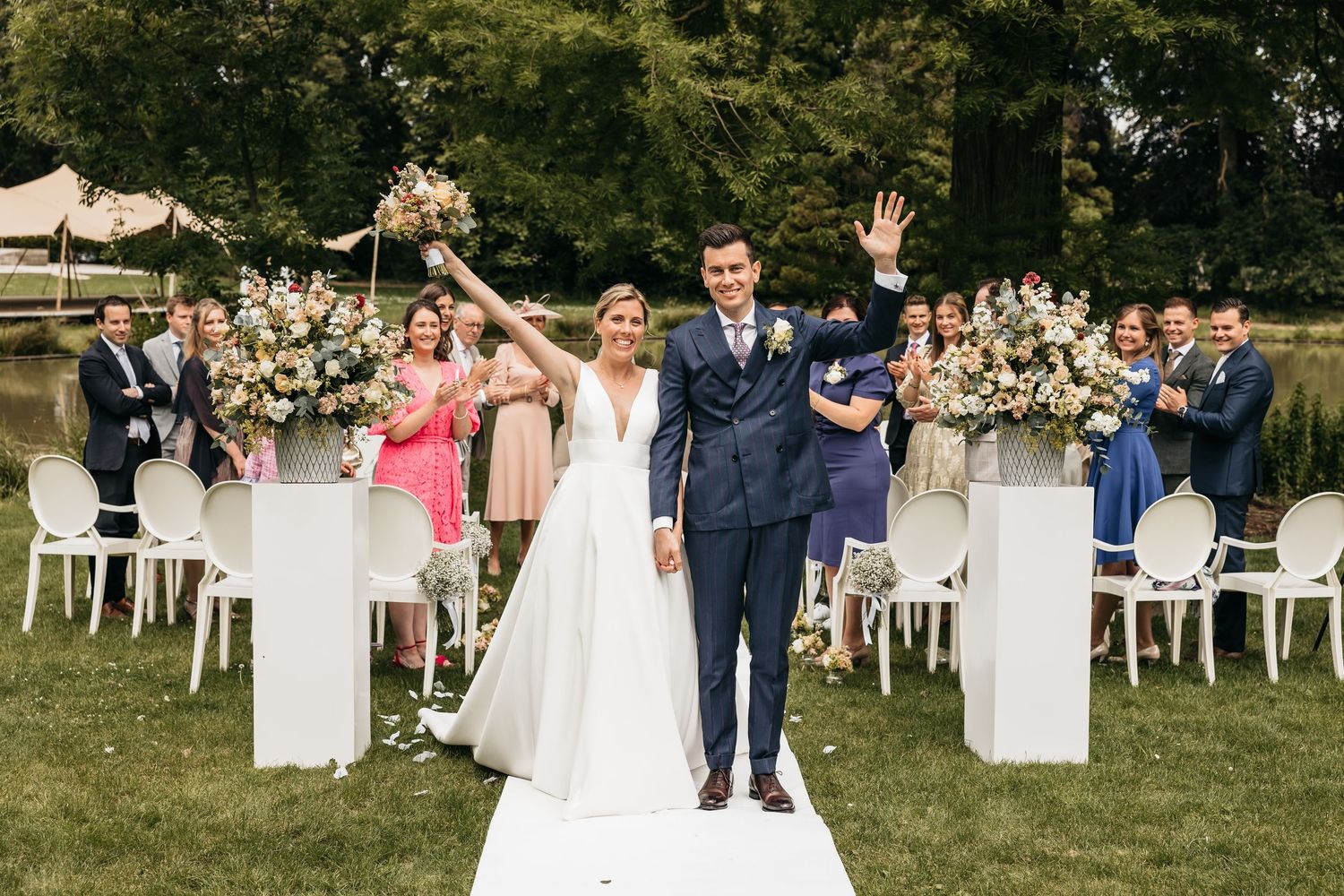 Joyful newlyweds celebrate with raised hands as guests cheer during outdoor wedding ceremony exit.