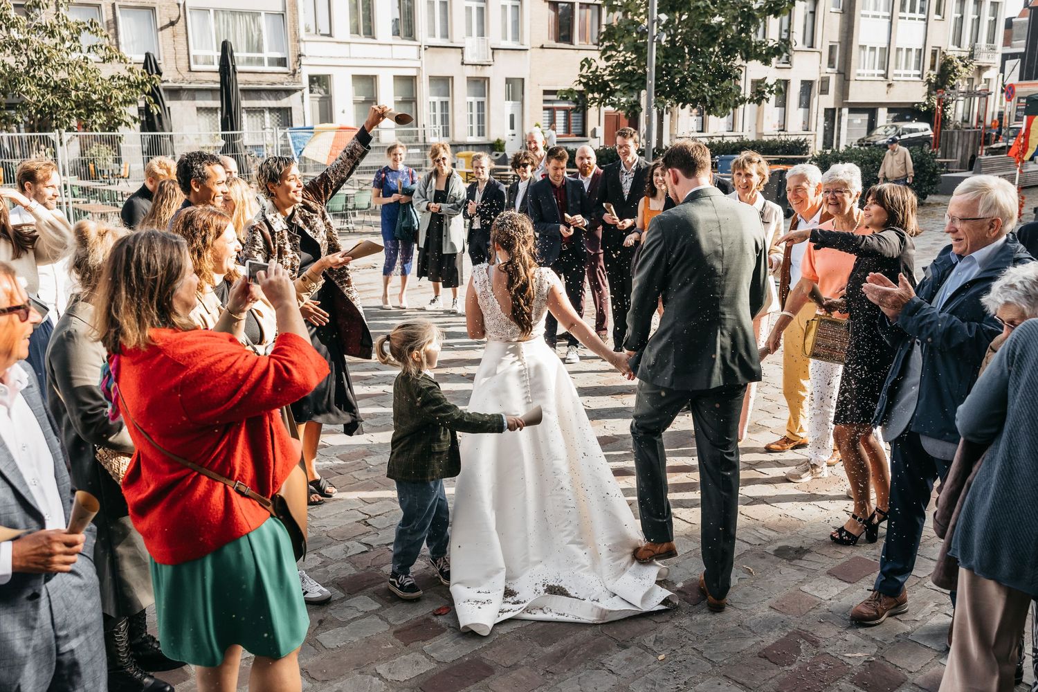 Newlyweds share joyful moment with young child guest in festive outdoor wedding celebration plaza.