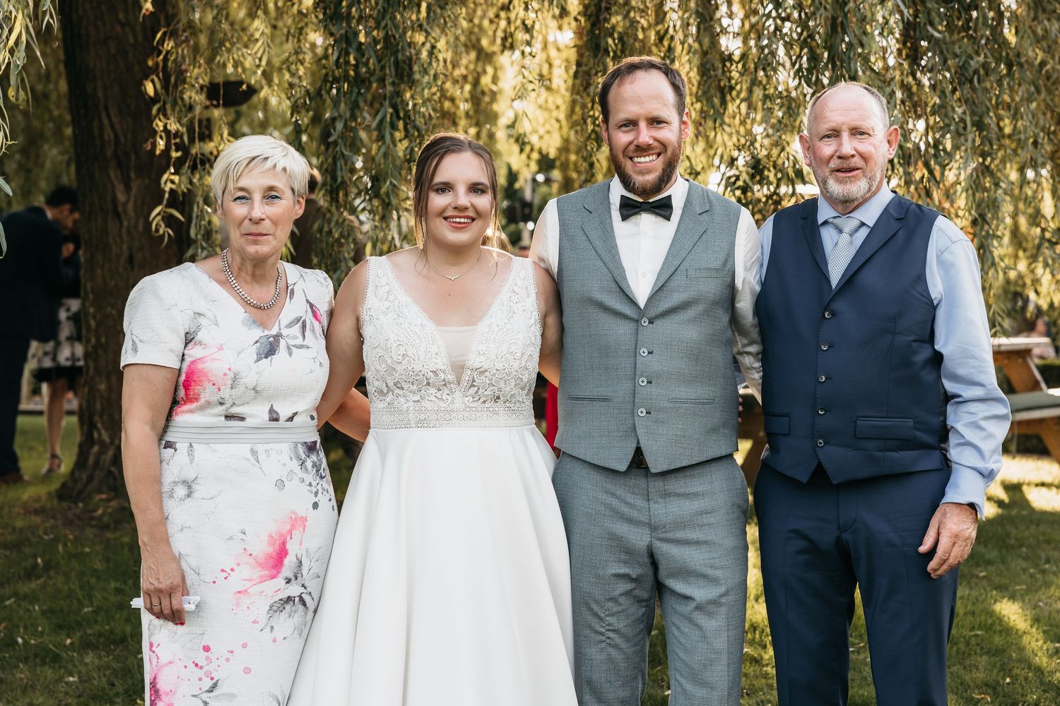 Bride and groom posing with two older family members under a willow tree at their wedding.