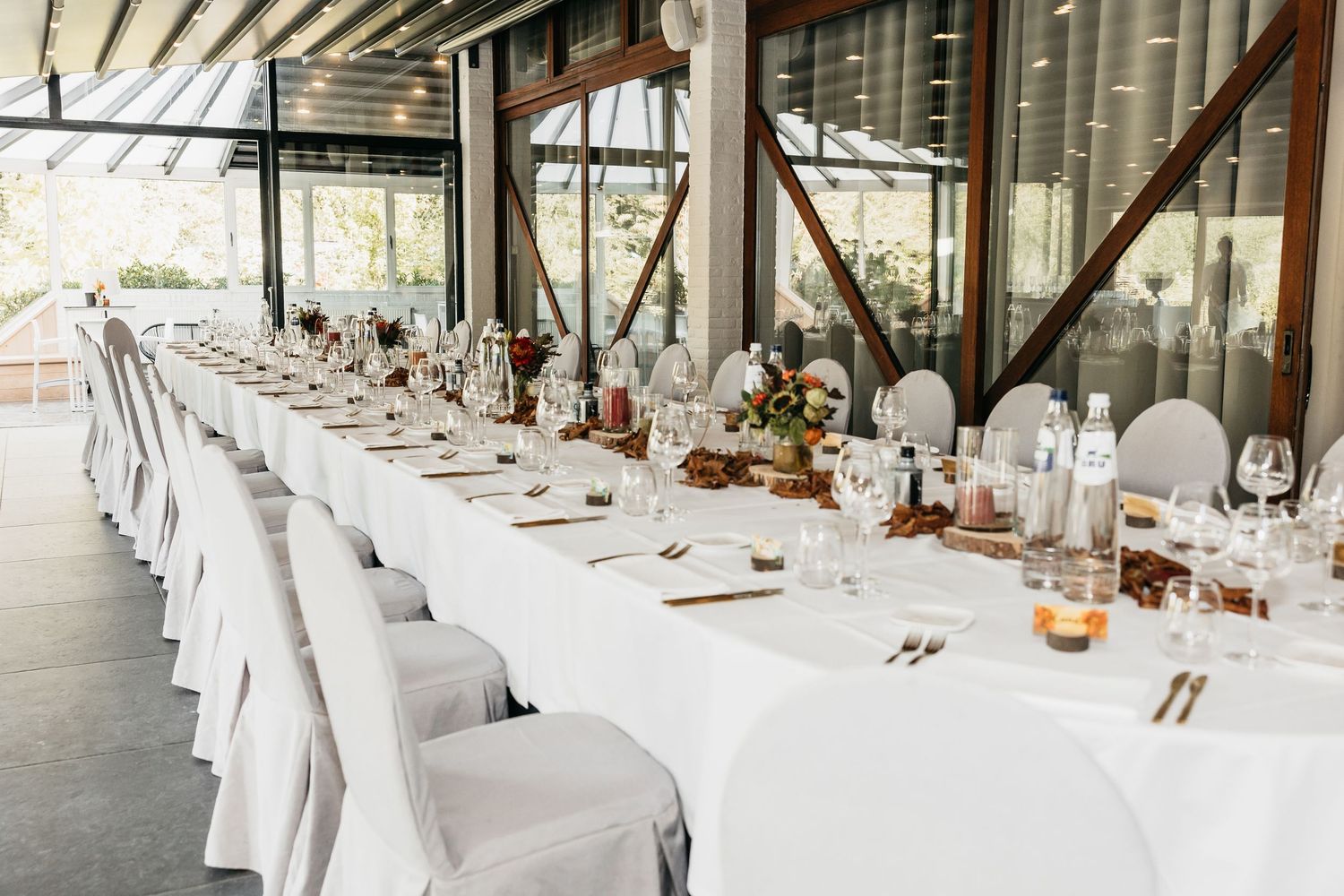 Long banquet table with white chair covers and autumn floral arrangements.