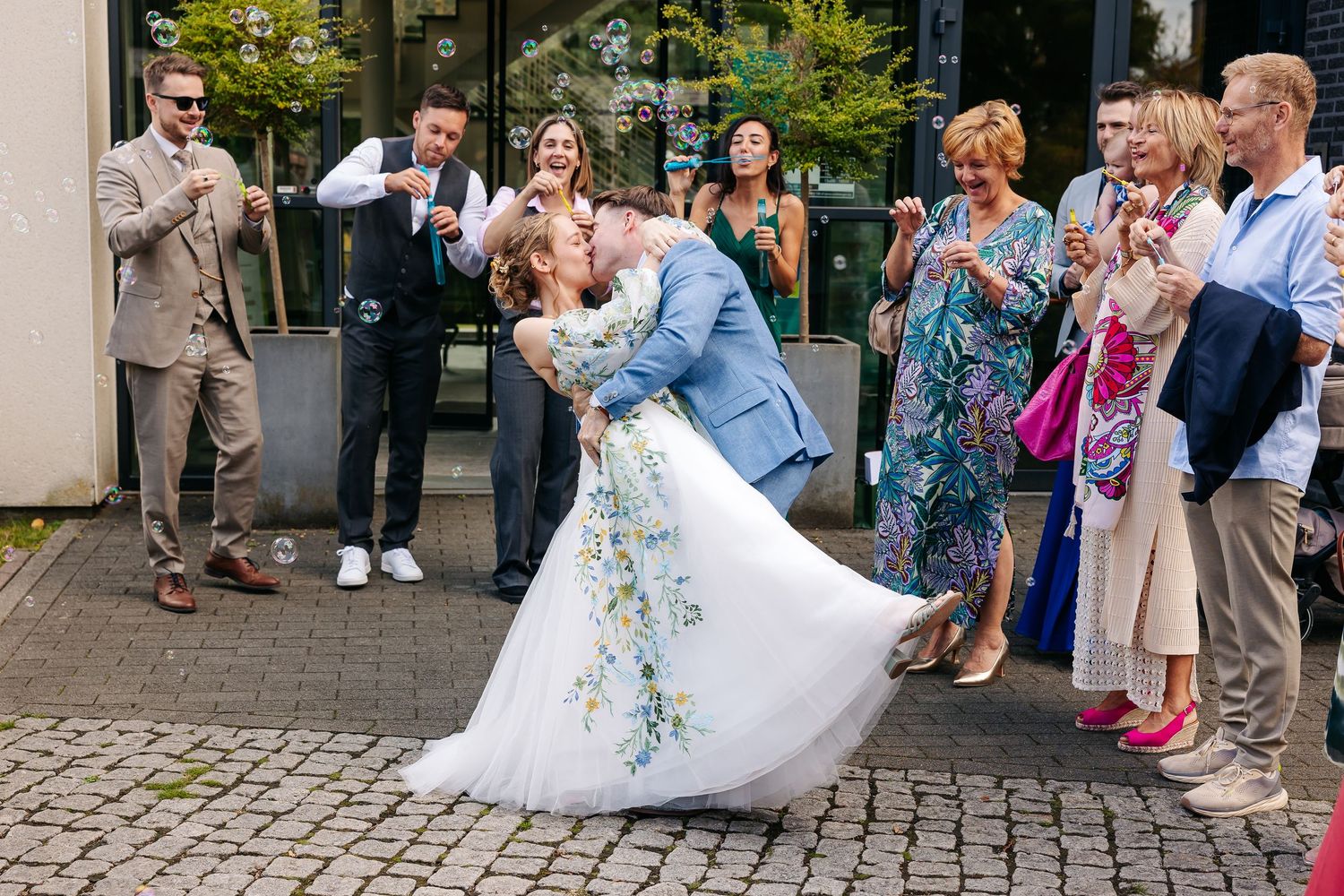 Groom dips bride in floral wedding dress for a romantic kiss outside wedding venue.