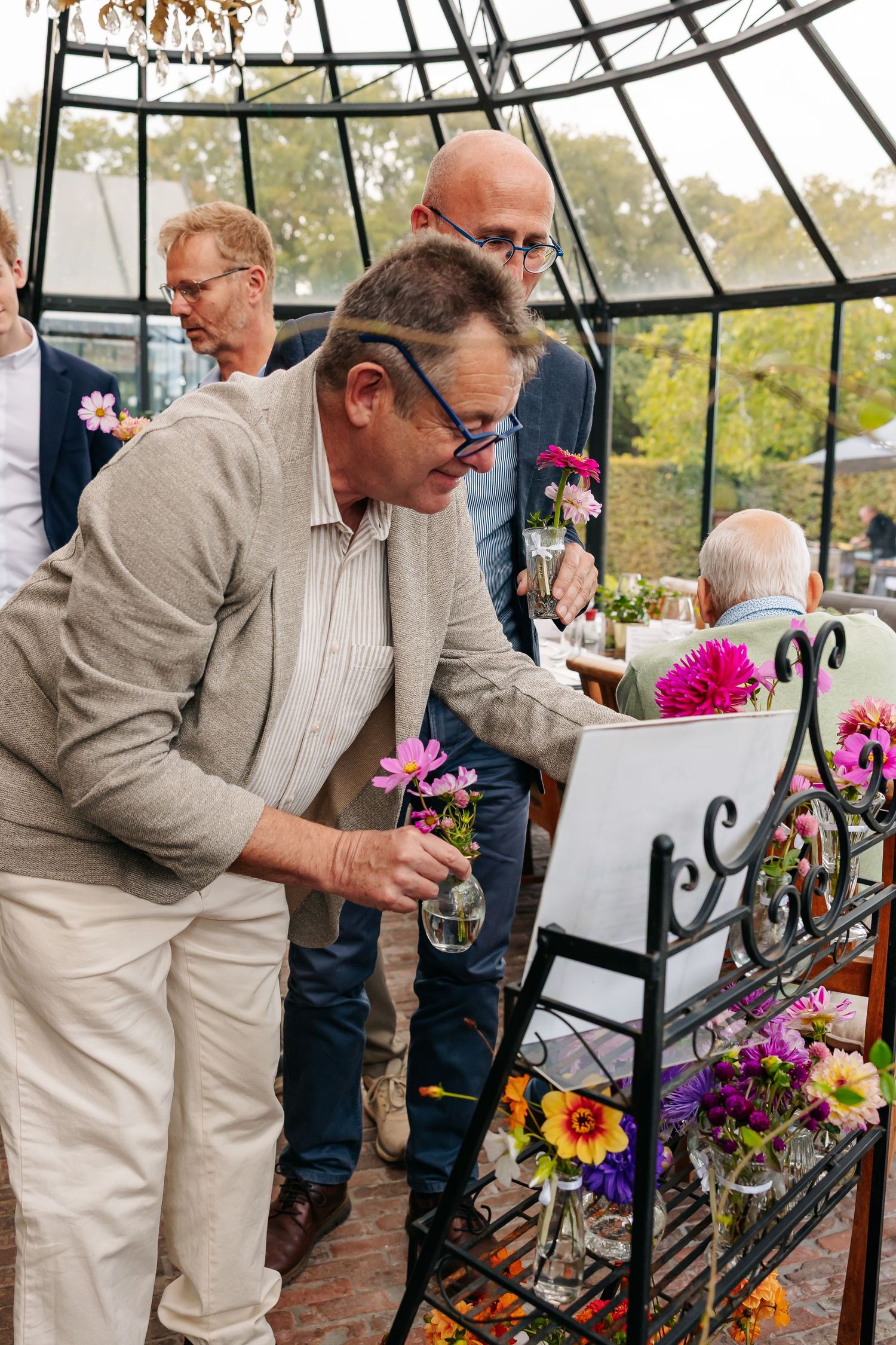 A man in a beige suit examines colorful floral arrangements inside a glass dome venue.
