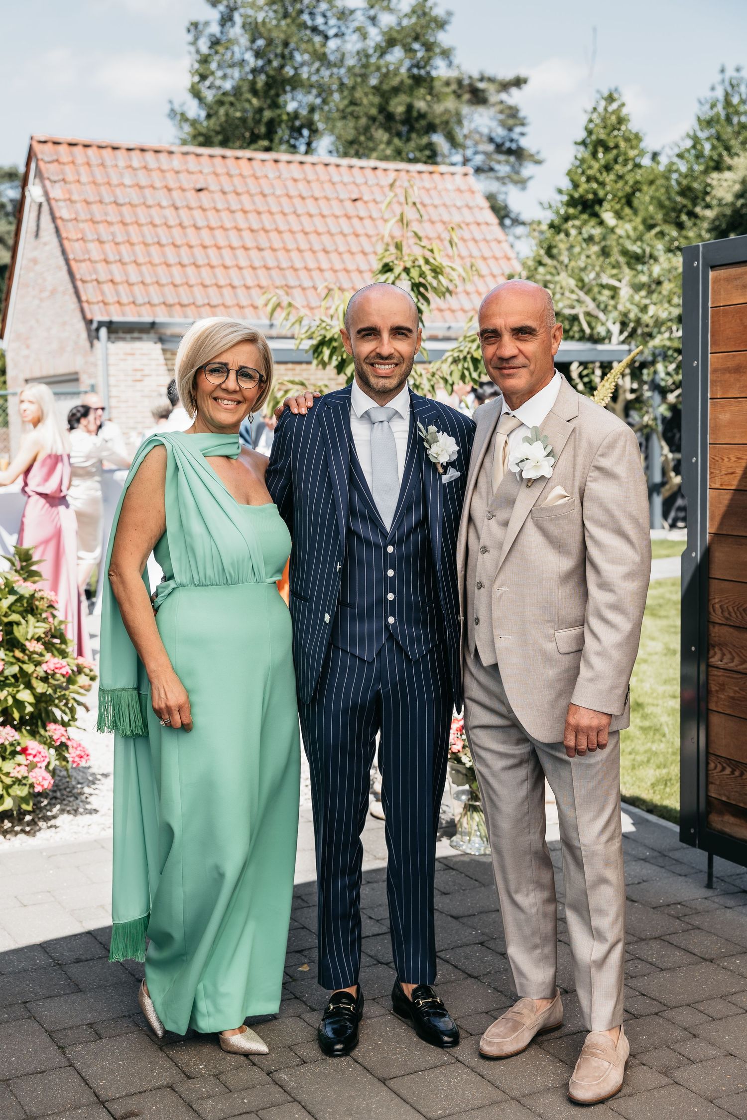 Groom in navy pinstripe suit posing with parents in teal dress and beige suit at wedding.
