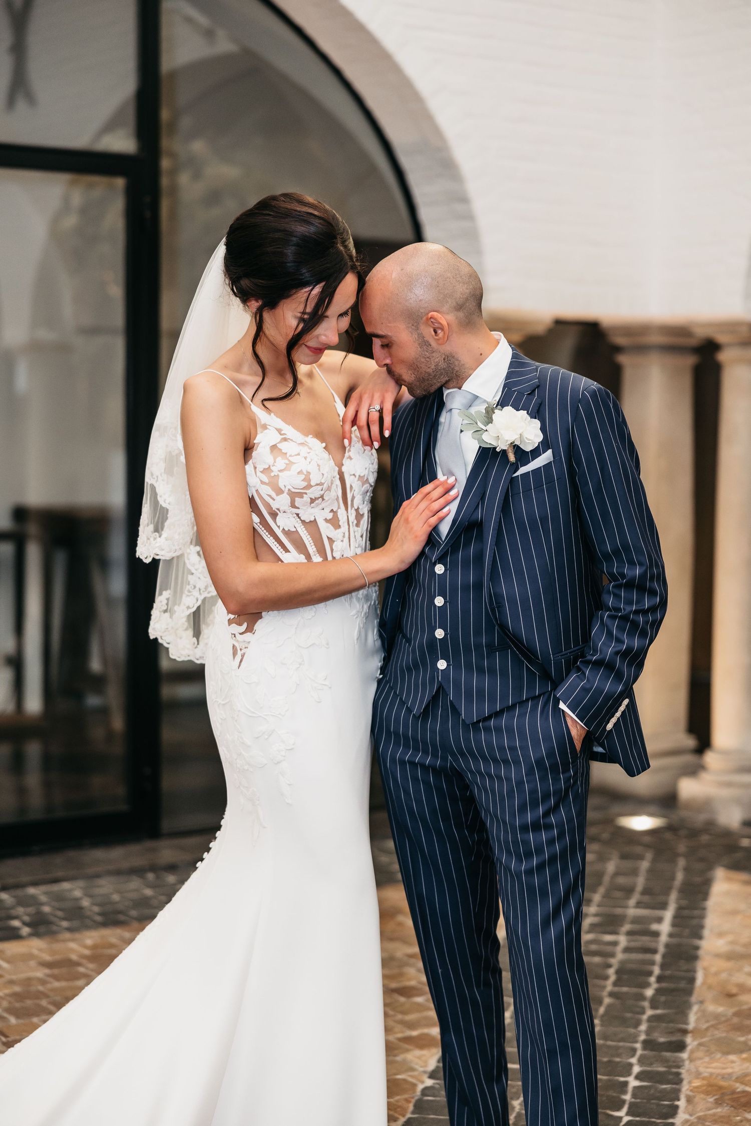 Bride and groom in navy pinstripe suit share intimate forehead touch during outdoor wedding portraits.