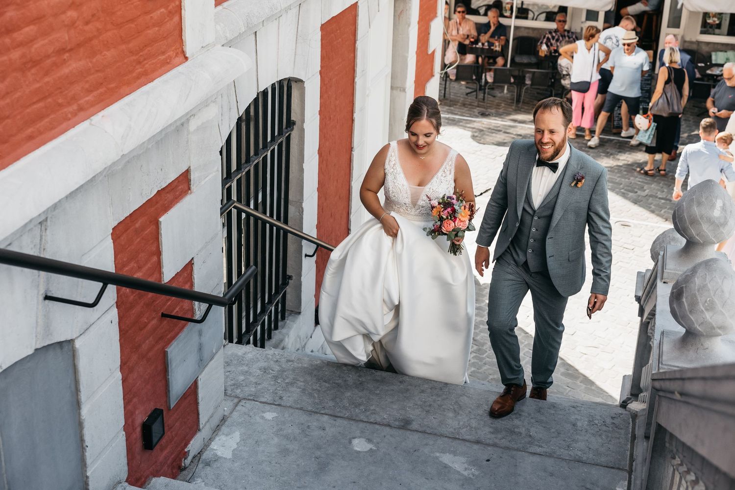 Bride and groom walking up outdoor steps, bride holding a bouquet in a white ball gown wedding dress.