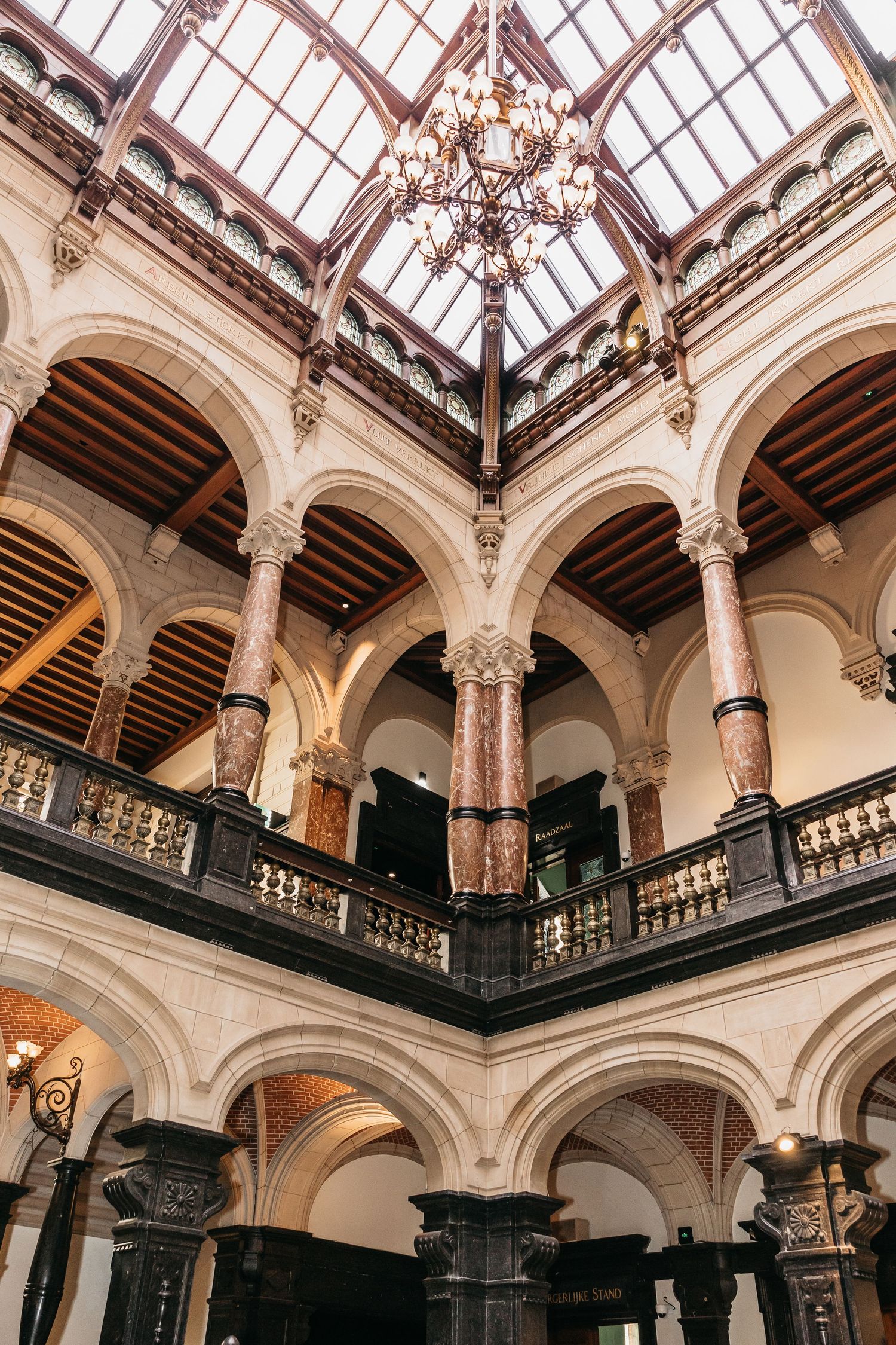 Elegant multi-story interior atrium with marble columns, arched balconies, and decorative glass skylight chandelier.