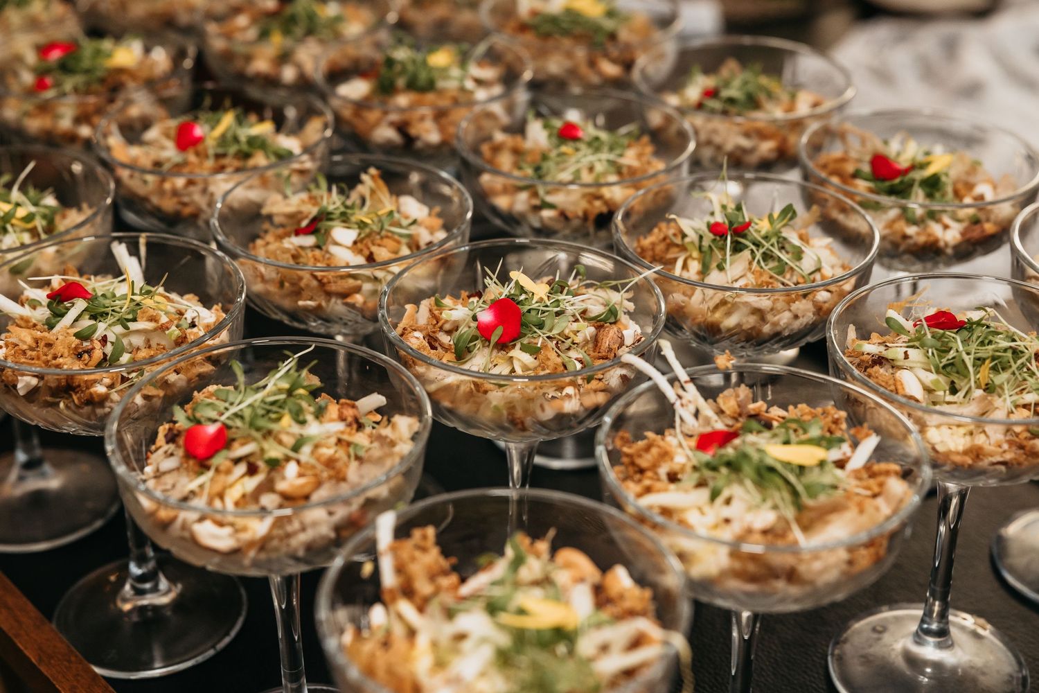 Elegant wedding appetizers served in martini glasses garnished with microgreens and red flowers at a reception.