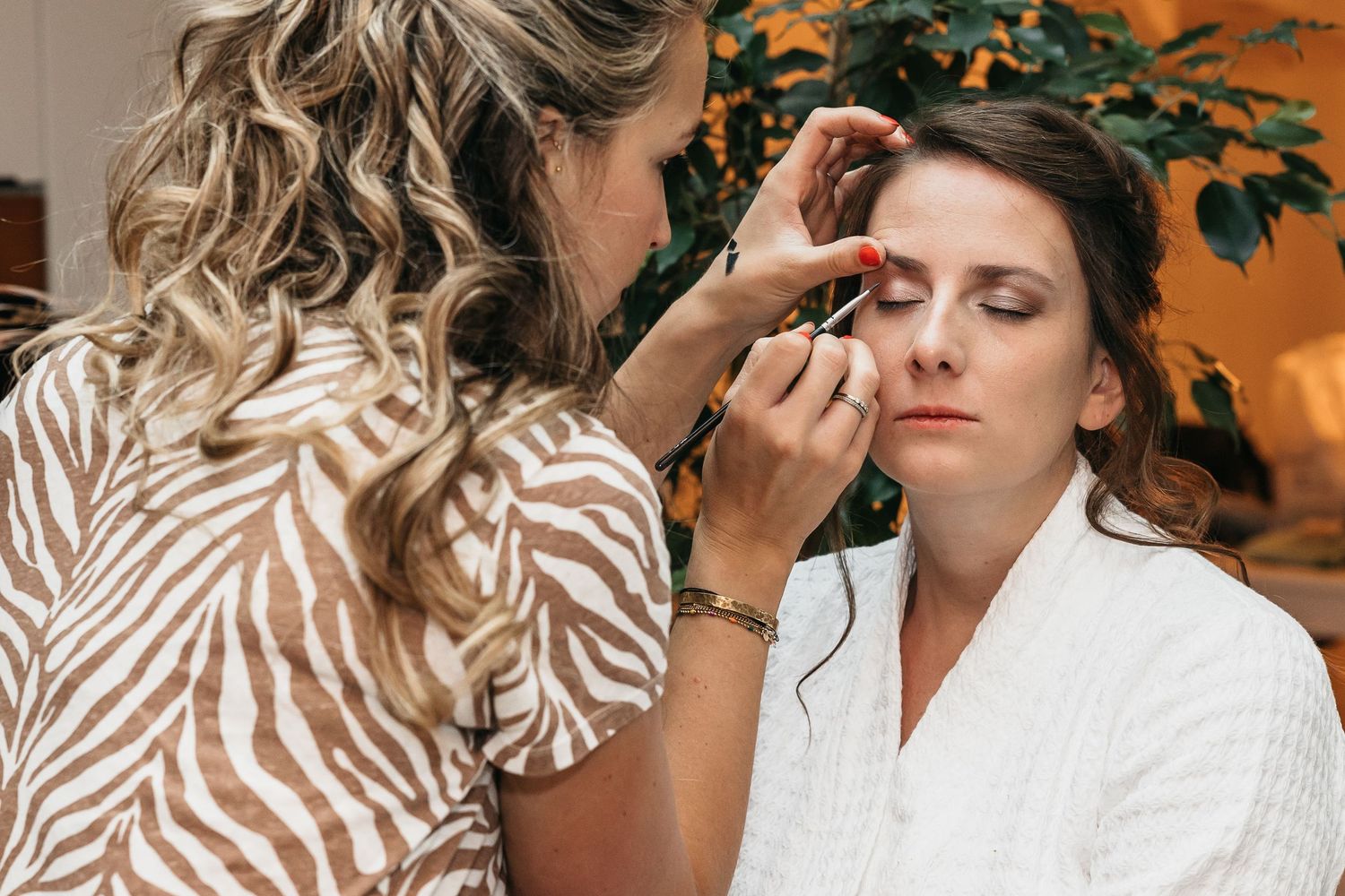 Close-up of makeup artist applying eyeshadow to a bride wearing a white robe.
