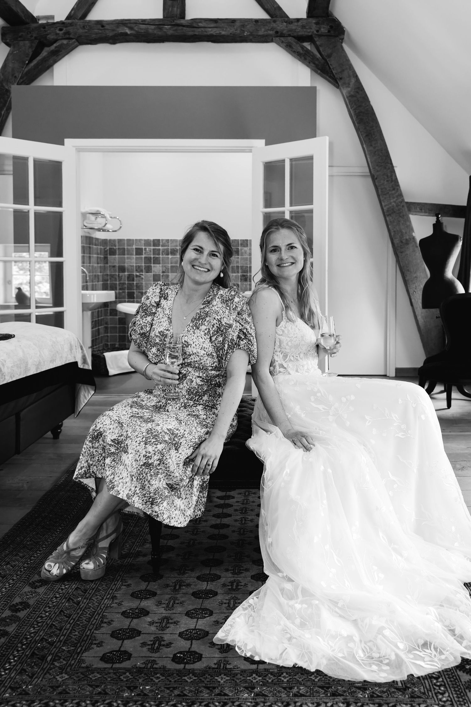 Black and white photo of bride in white gown and guest sitting together smiling in rustic room.