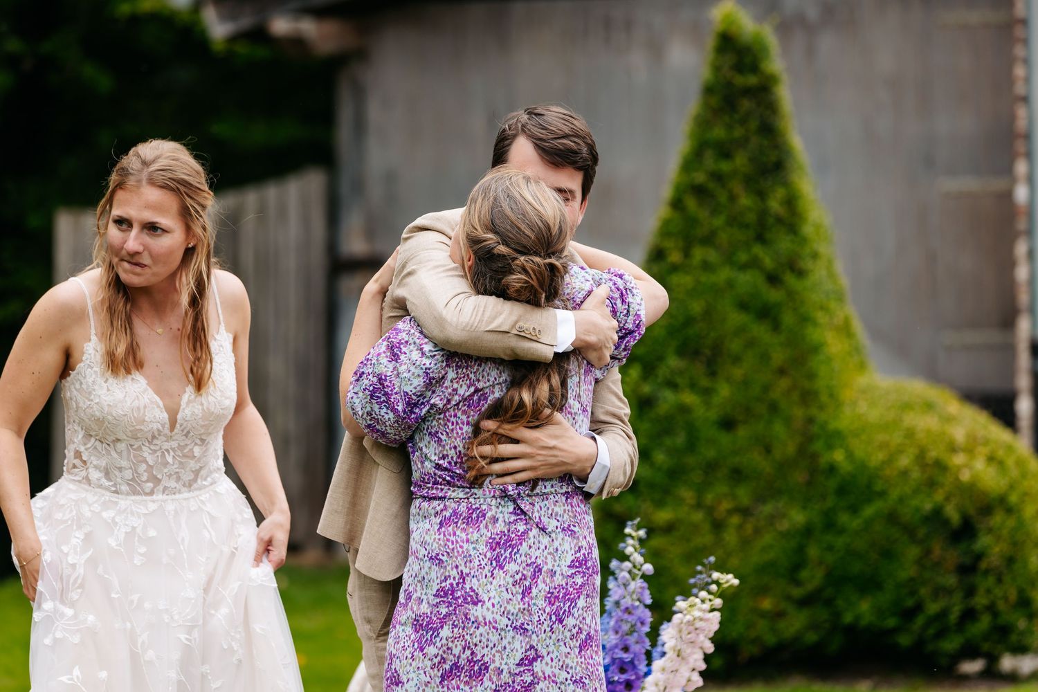 Groom sharing emotional hug with guest in purple floral dress after wedding ceremony.