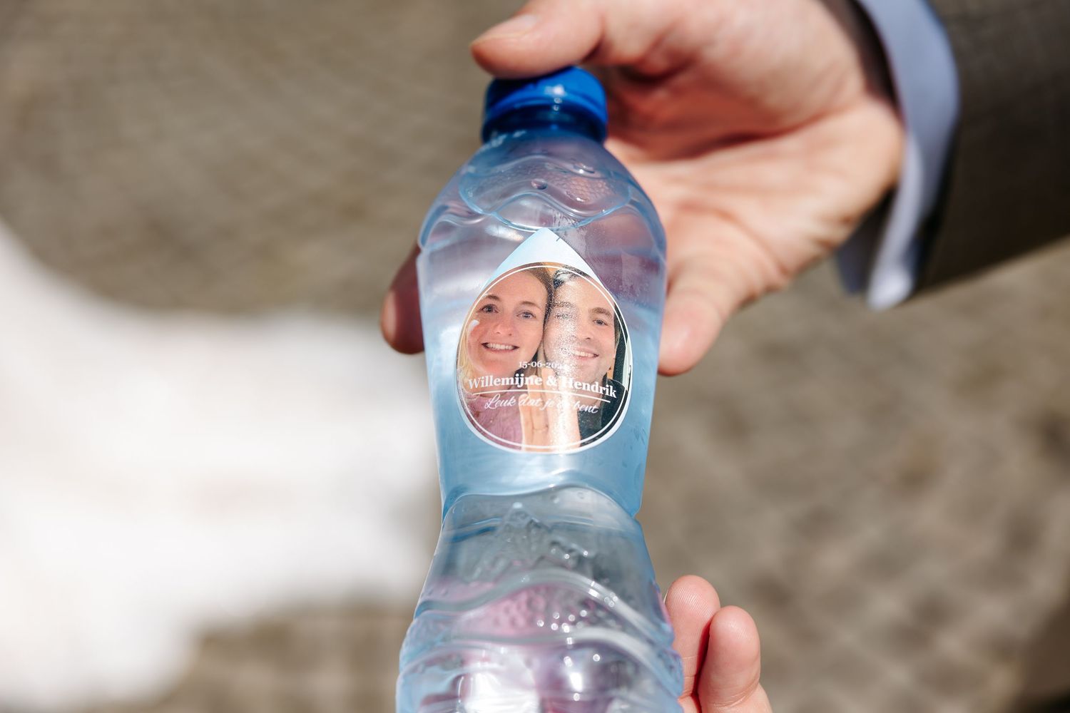 Custom wedding water bottle label featuring smiling couple portrait held up close to camera.