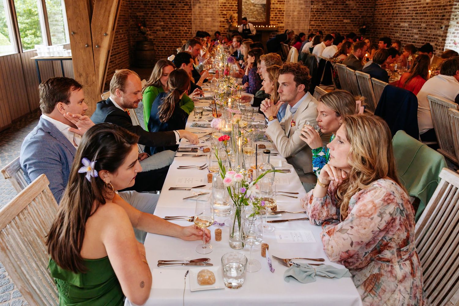 Wedding guests seated at long decorated tables enjoying a reception dinner indoors.