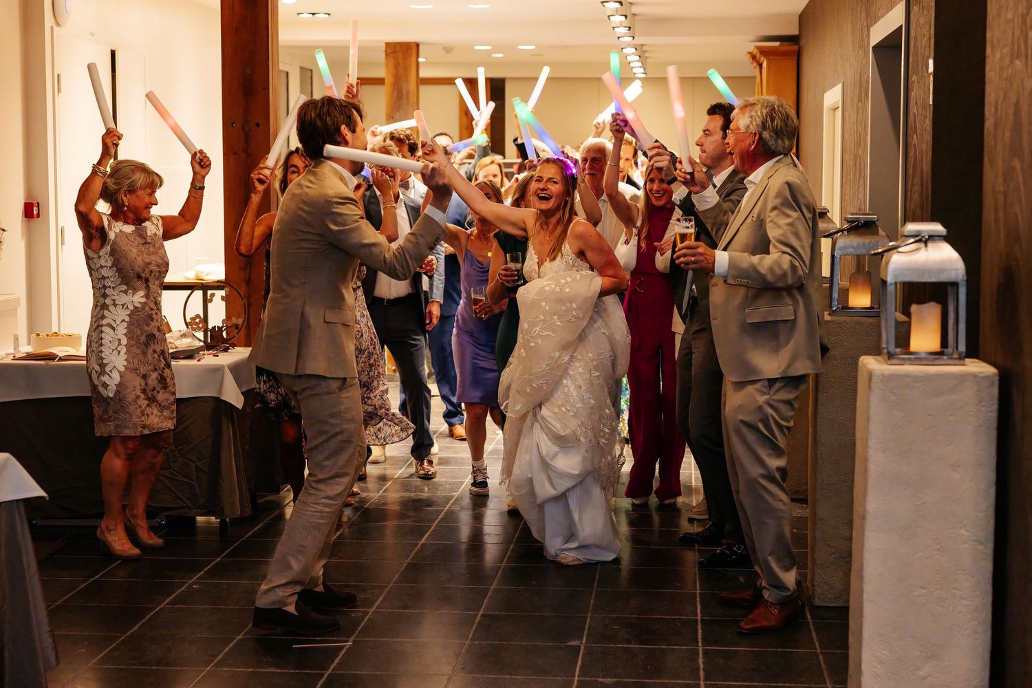 Bride and groom walk through a tunnel of glowing light sticks held by cheering wedding guests.