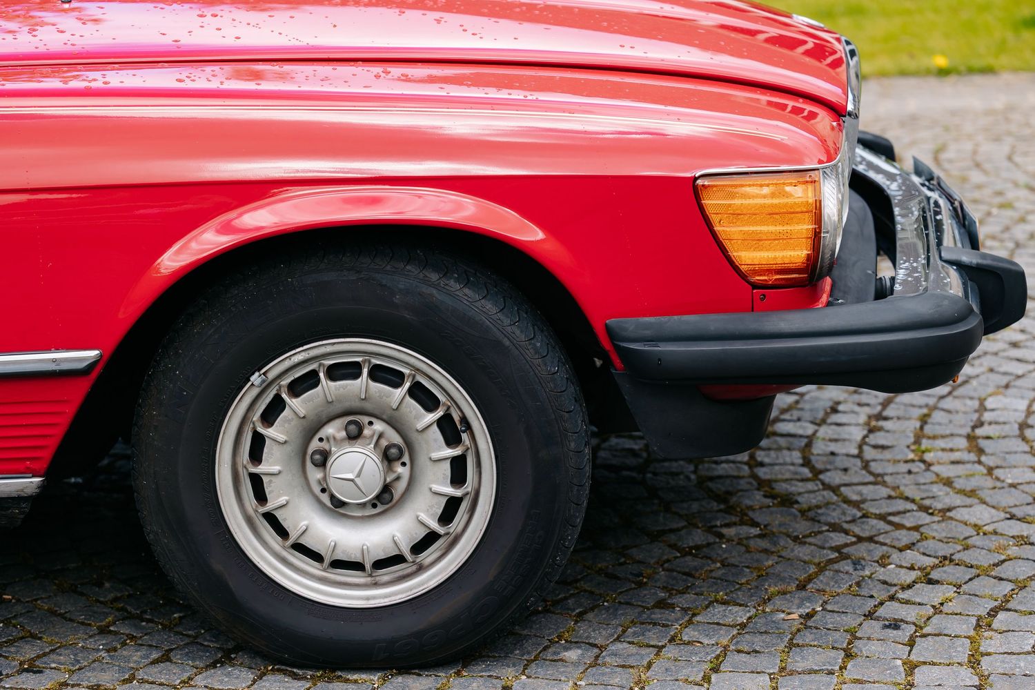 Close-up of a classic red Mercedes-Benz SL with alloy wheel on cobblestone.