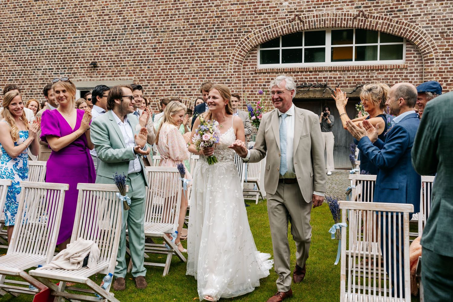 A radiant bride walks the aisle with her father as smiling guests celebrate at an outdoor wedding.