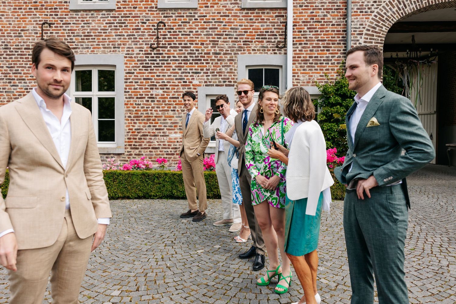 Wedding guests in elegant attire socializing on cobblestone courtyard outside brick venue.