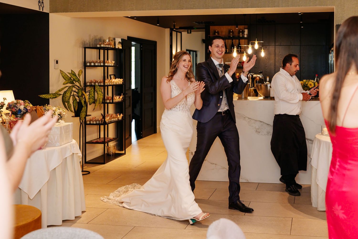 Bride and groom make grand entrance at wedding reception while guests applaud in elegant venue.