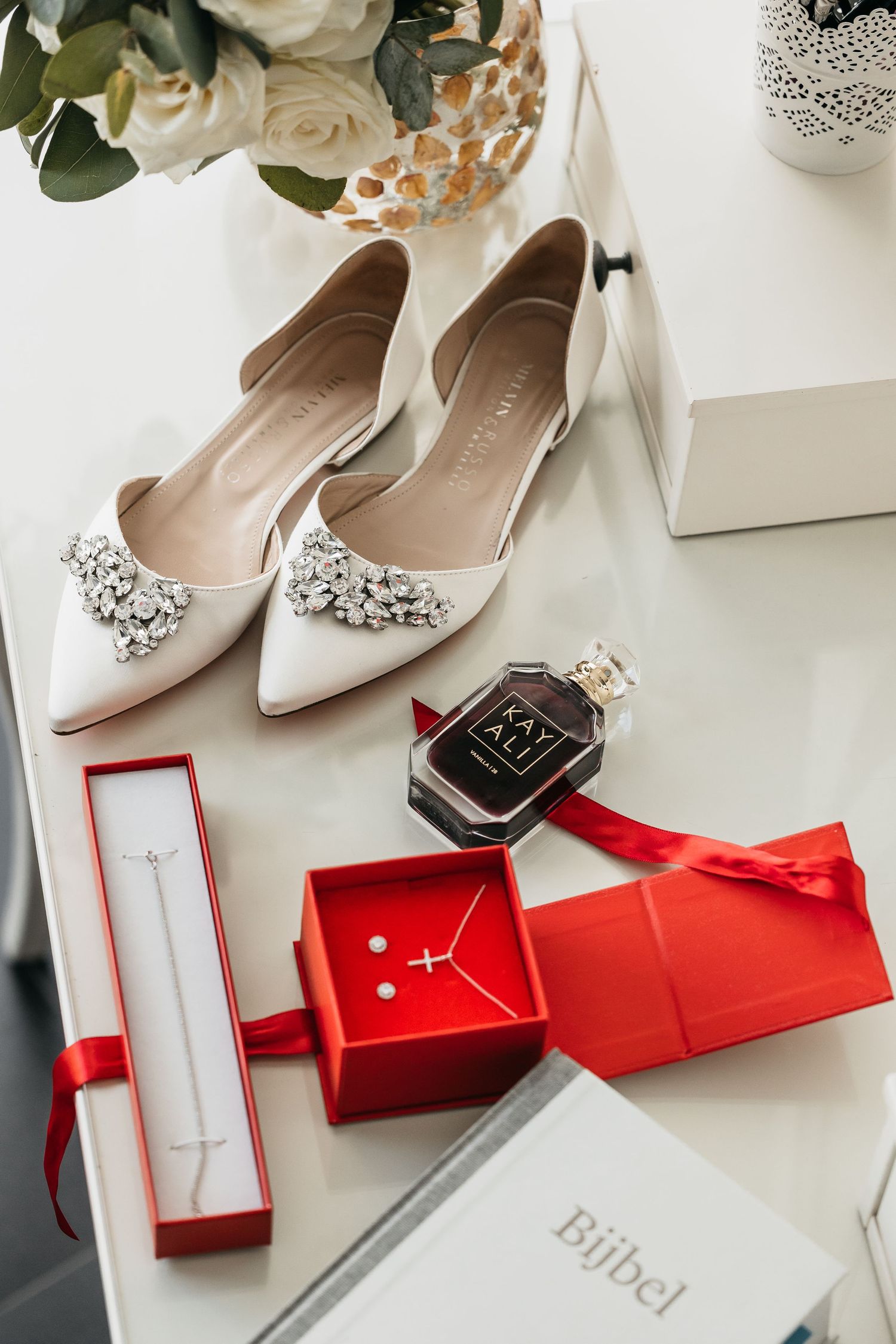 White jeweled bridal flats with Kayali perfume, cross necklace, and Bijbel on vanity.